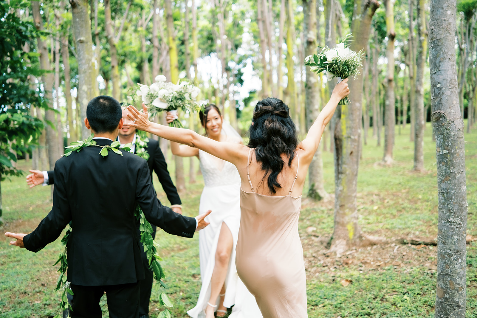 Newlyweds walking down a tree-lined path, greeted by cheers from joyful guests captured by Oahu Wedding Photographer