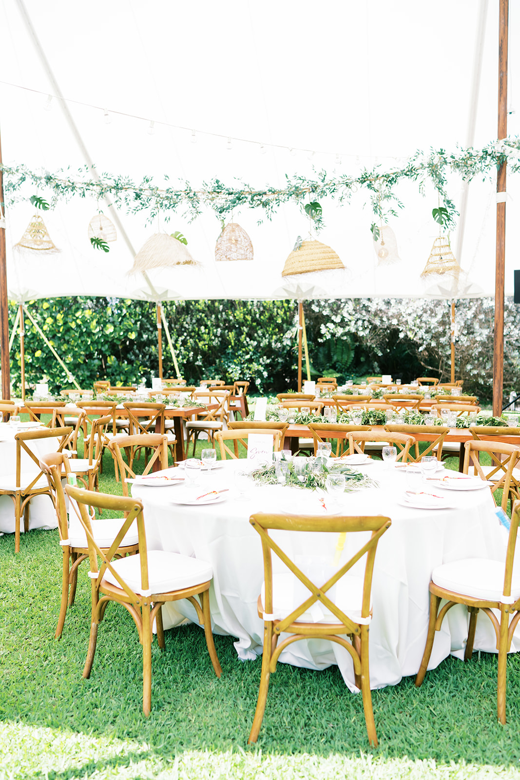 Outdoor dining setup for an event with wooden chairs and tables covered with white linens Wedding at Na Aina Kai