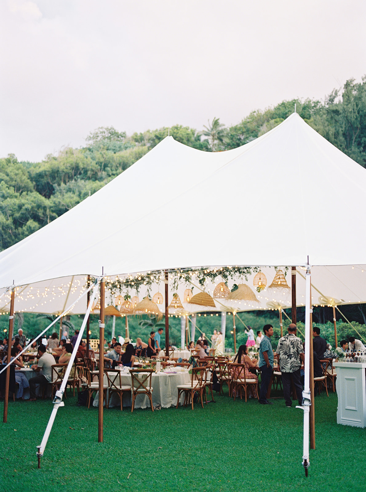 Outdoor event under a white canopy tent with string lights and guests seated at tables on a Wedding in Kauai