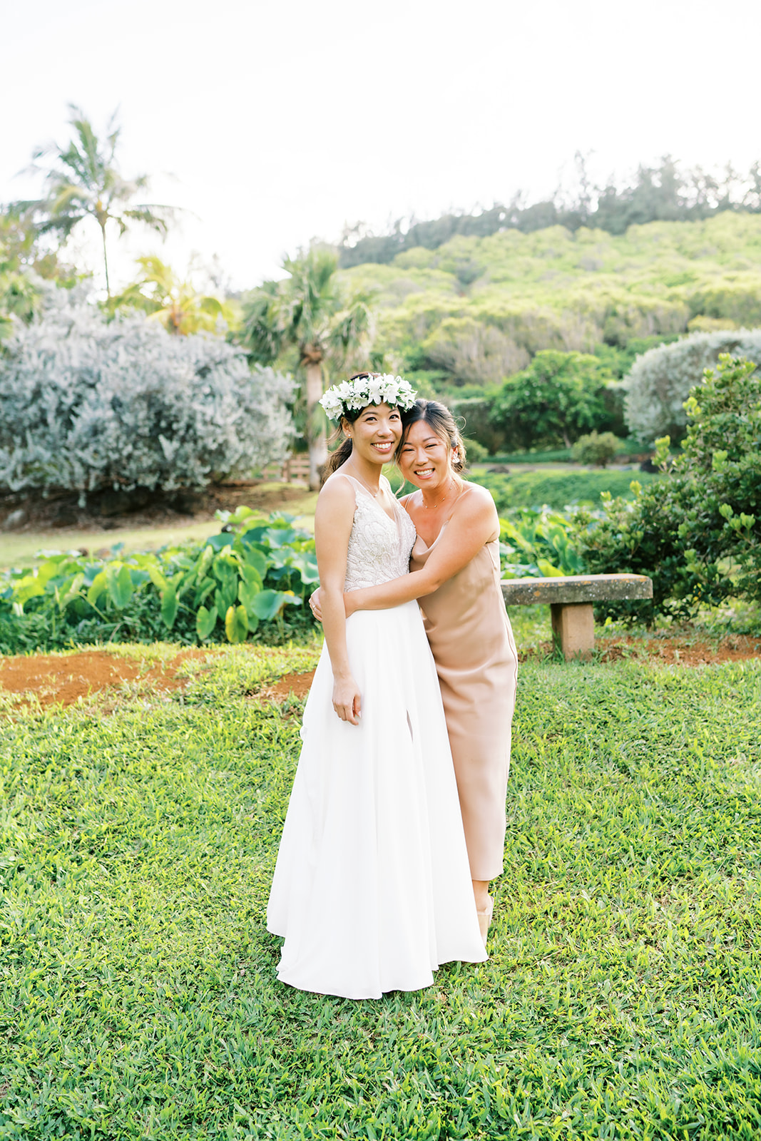 Two women smiling and embracing wearing formal attire, during wedding at Na Aina Kai Botanical Gardens