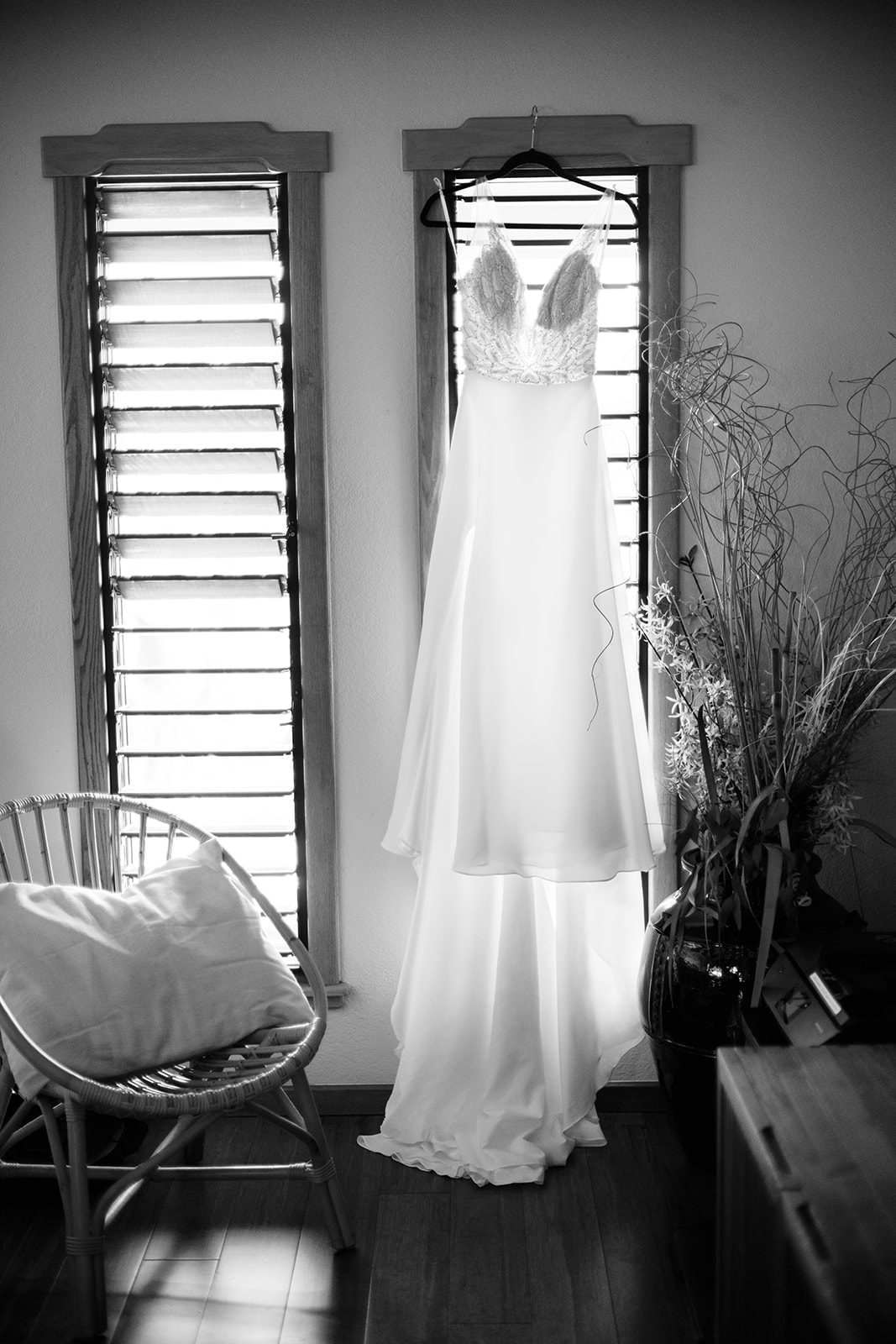 A wedding dress hanging in front of a window, casting a silhouette against the light filtering through blinds.