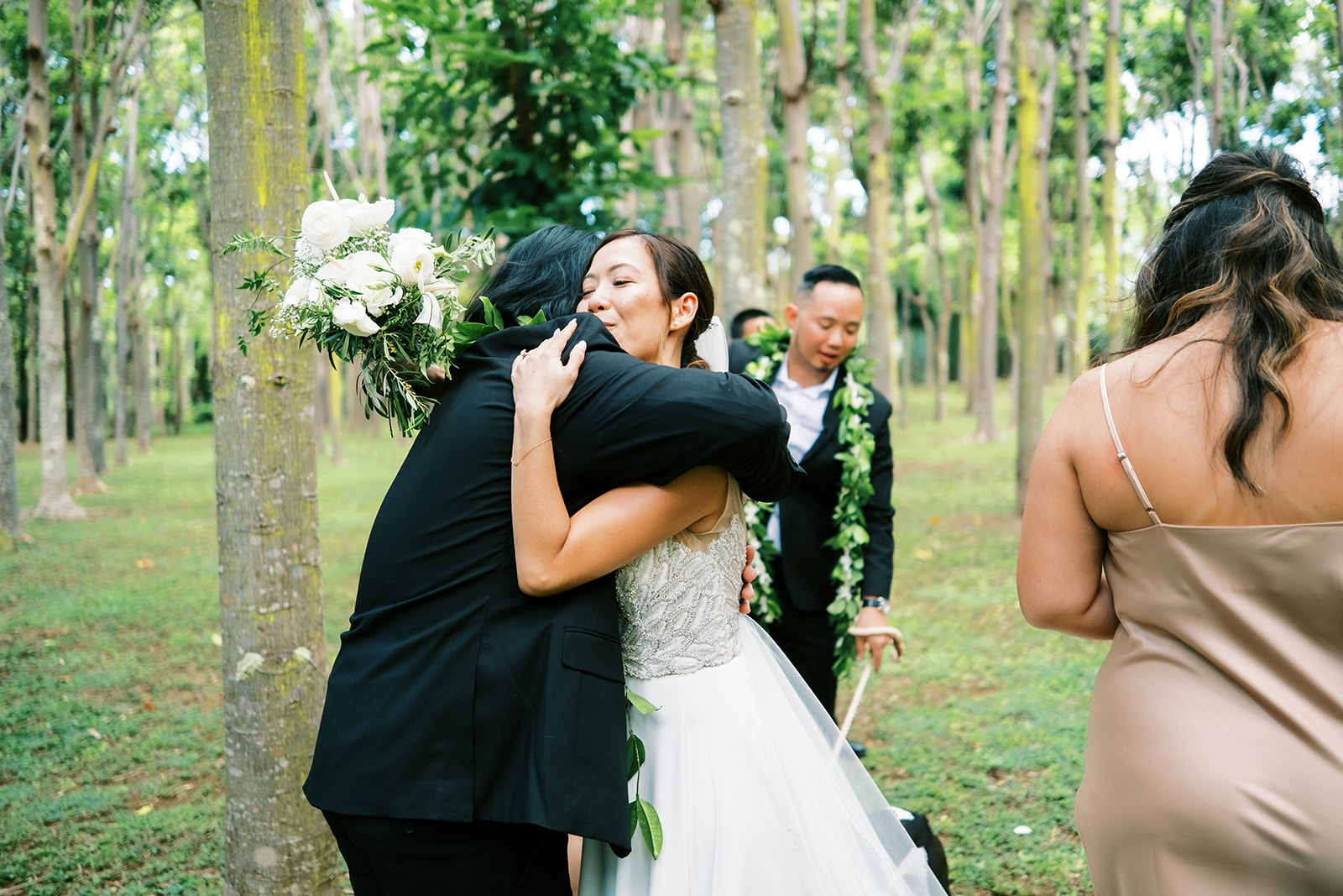 Wedding guest embracing a smiling bride in a forested area captured by Oahu Wedding Photographer
