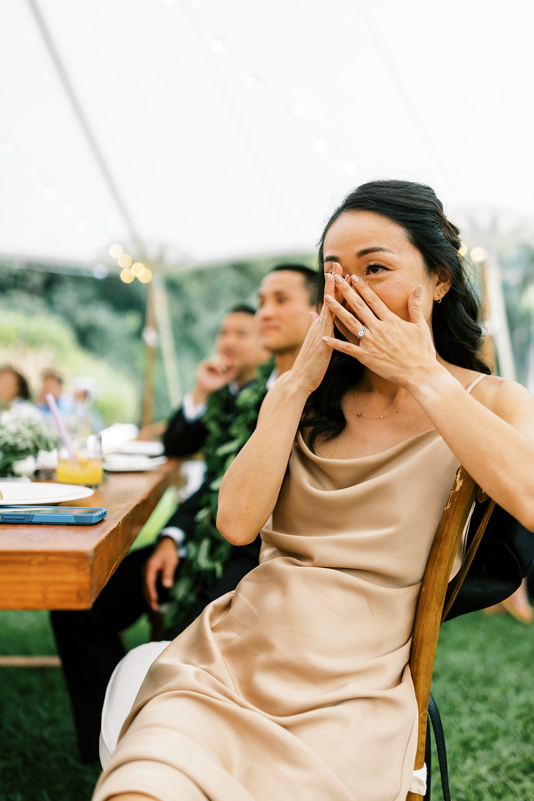 Woman in a beige dress wiping her tears of joy with her hand at a Wedding at Na Aina Kai