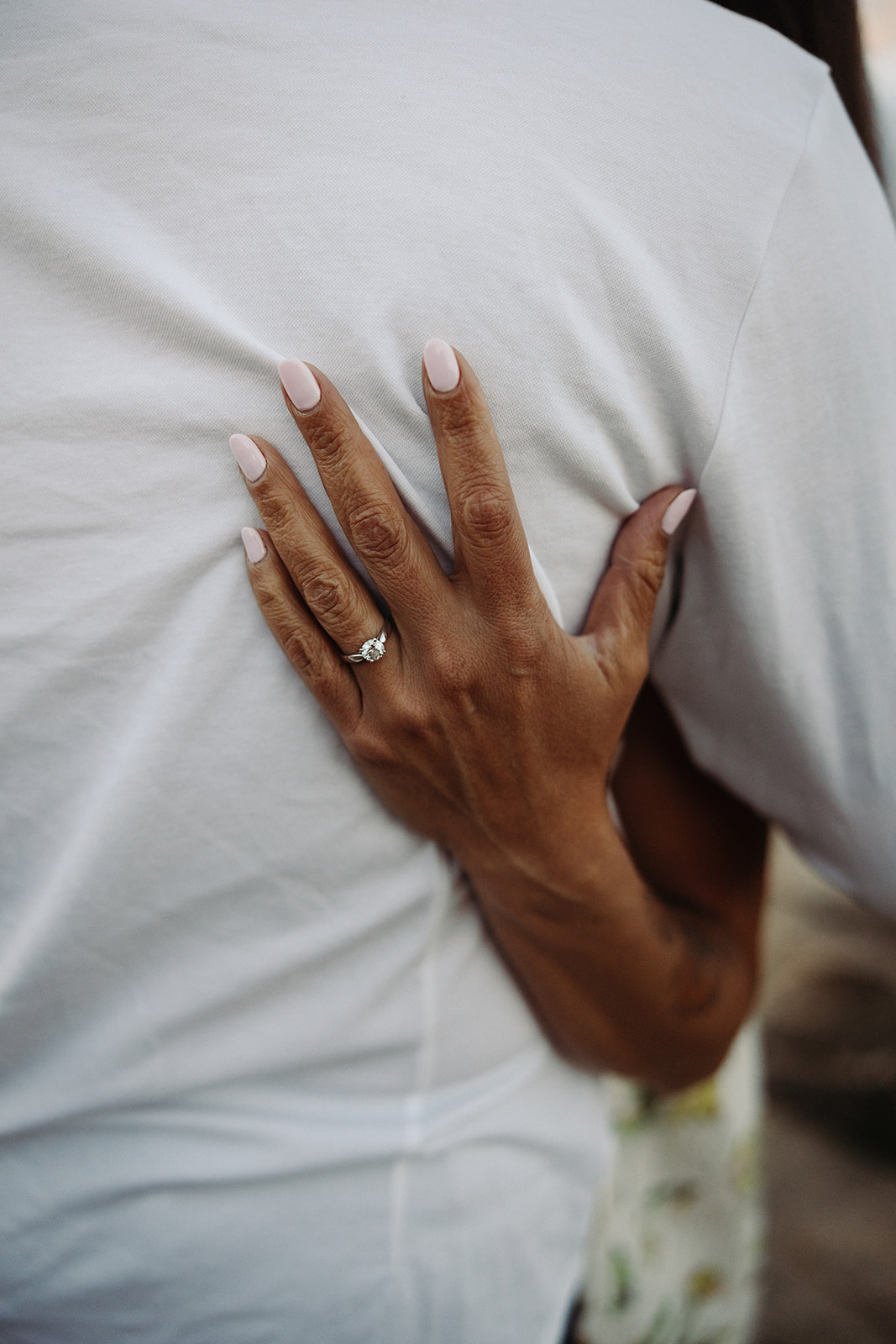 Woman's hand holding man's back showing her engagement ring