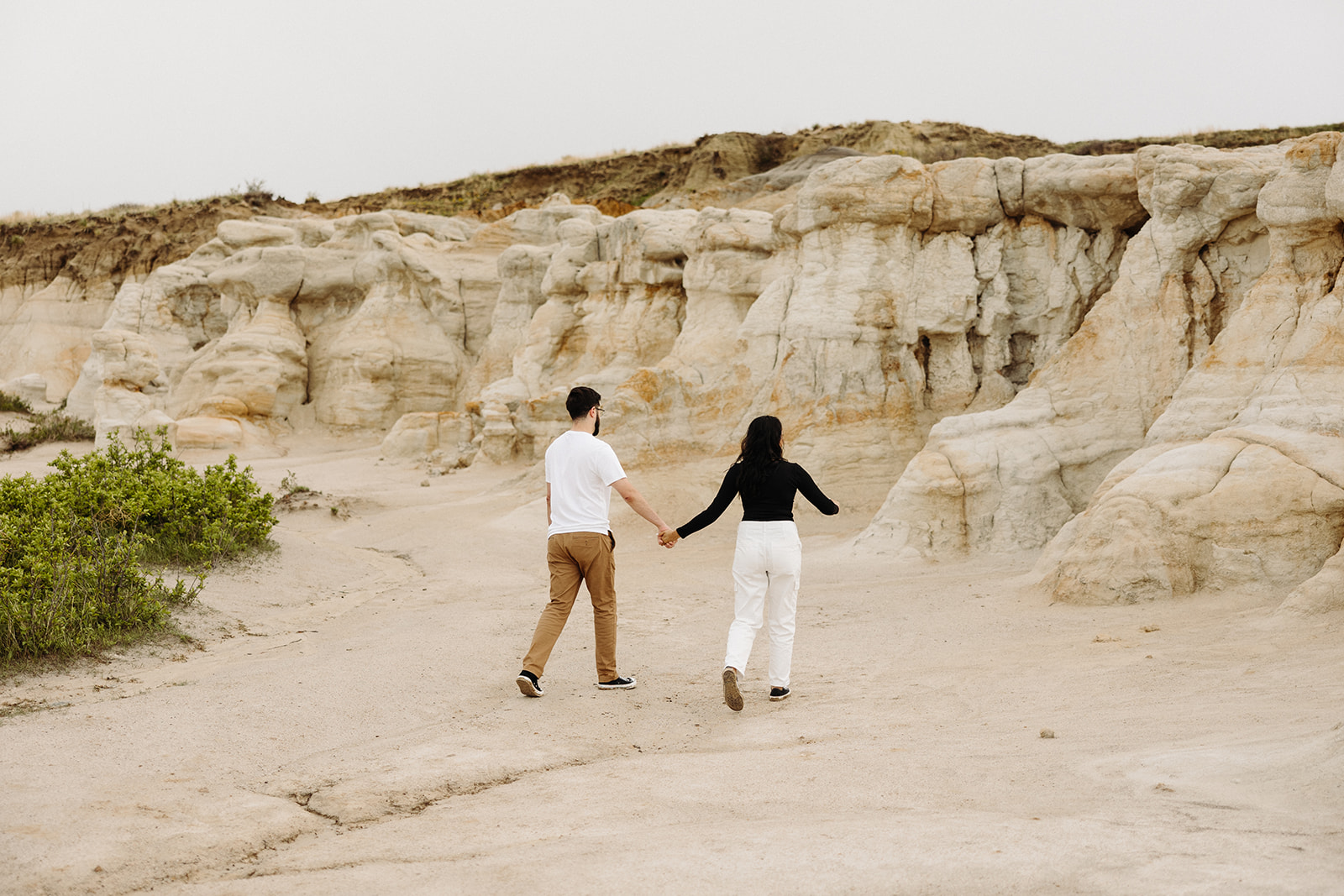 Man and woman holding hands and walking along a mountain during their Mountain Engagement 