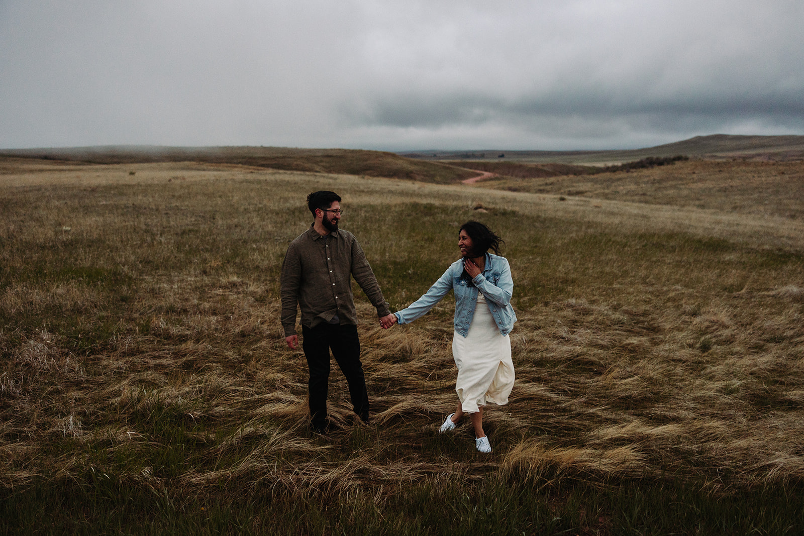 Man and woman holding hands while walking through a field during their Mountain Engagement 
