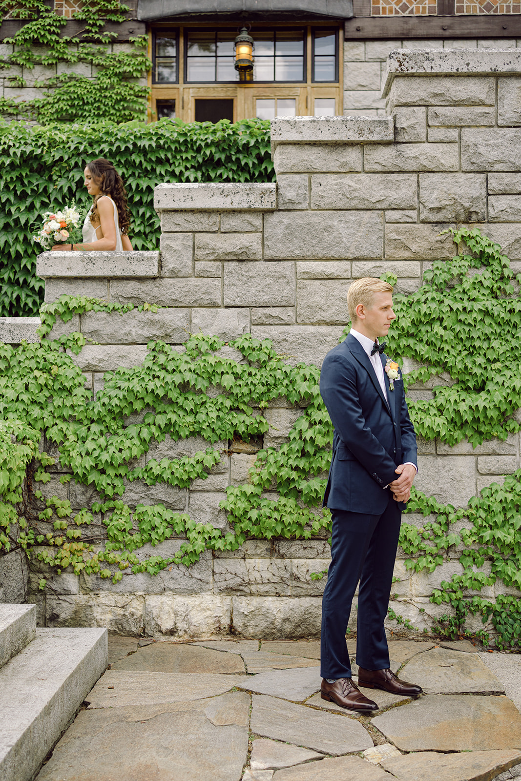 Groom wearing Senszio waits for his bride on the steps at their Blaylock Mansion wedding in Nelson BC