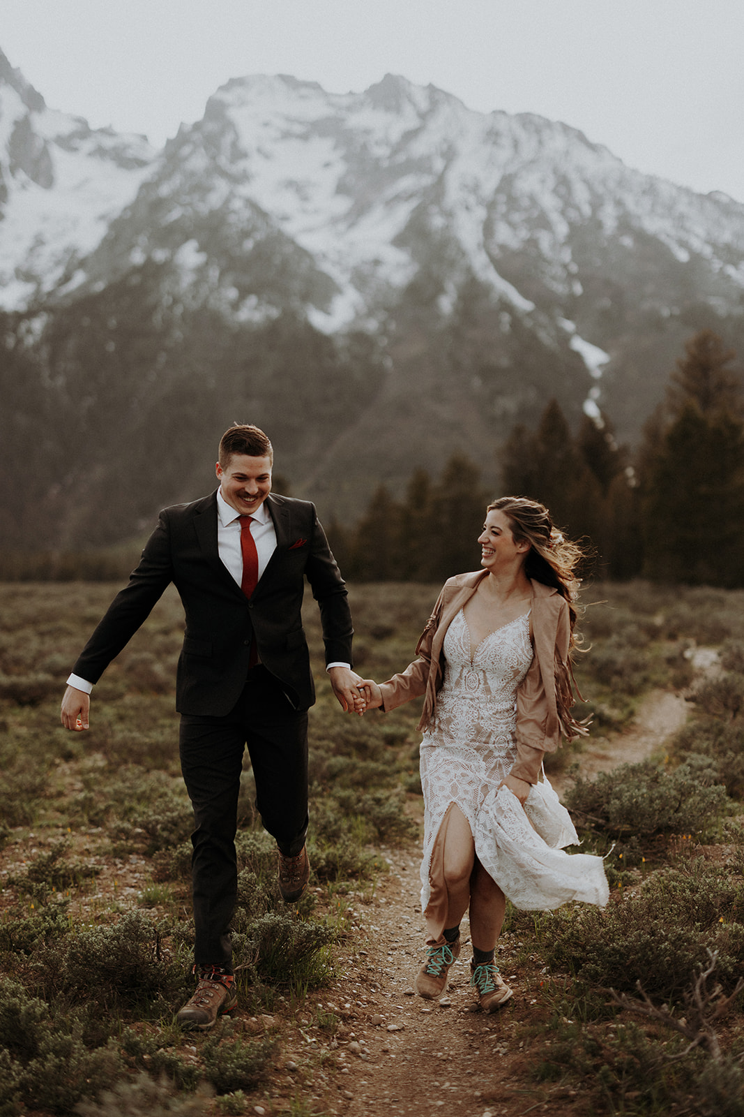 A boho wedding couple running along a path in Grand Teton  National Park.