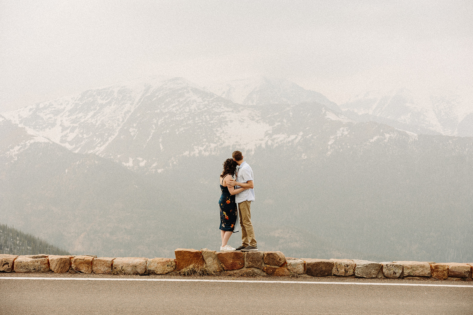 A man and woman hugging while standing on a ledge looking at the mountain view