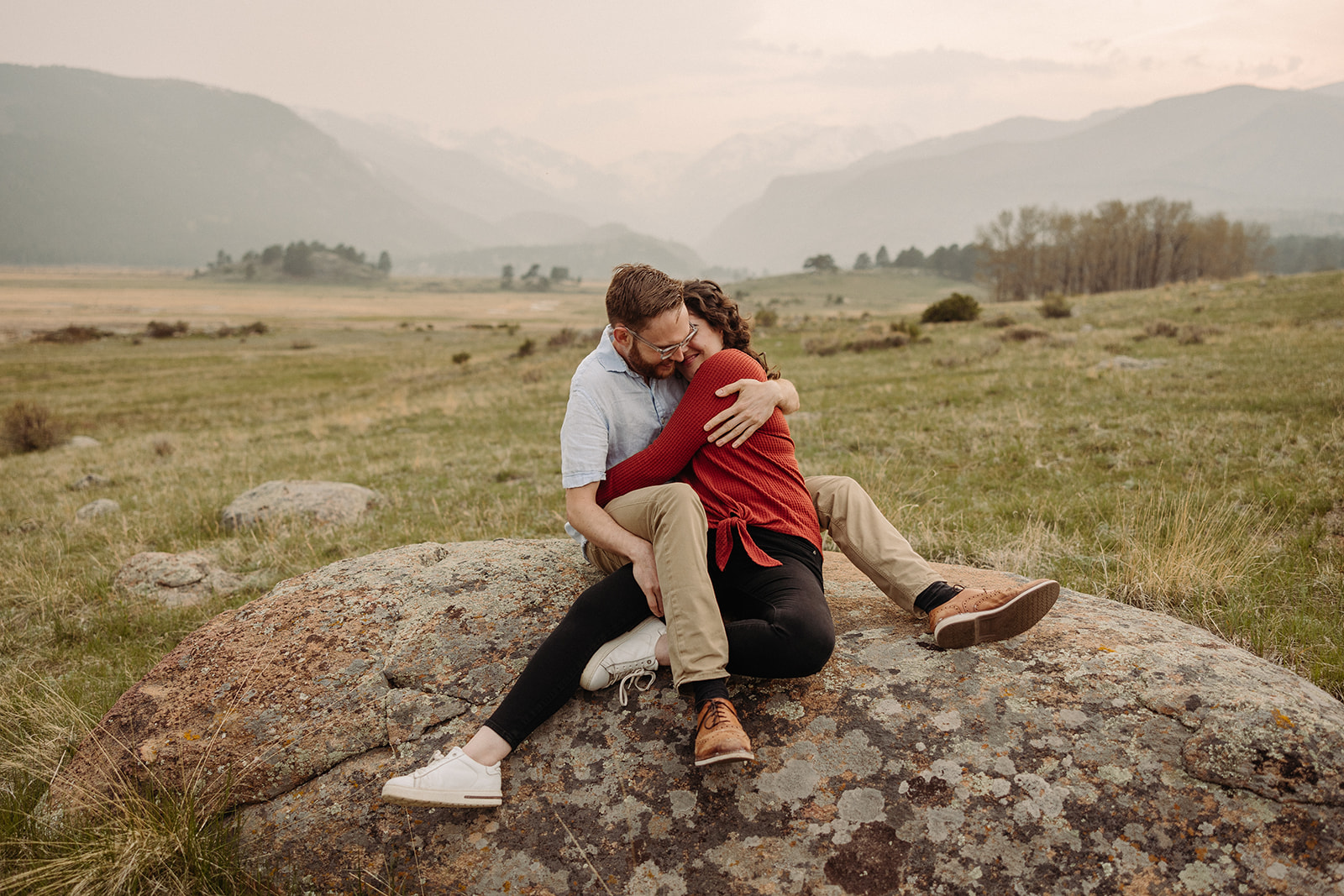 A man and woman hugginh while sitting on a big rock