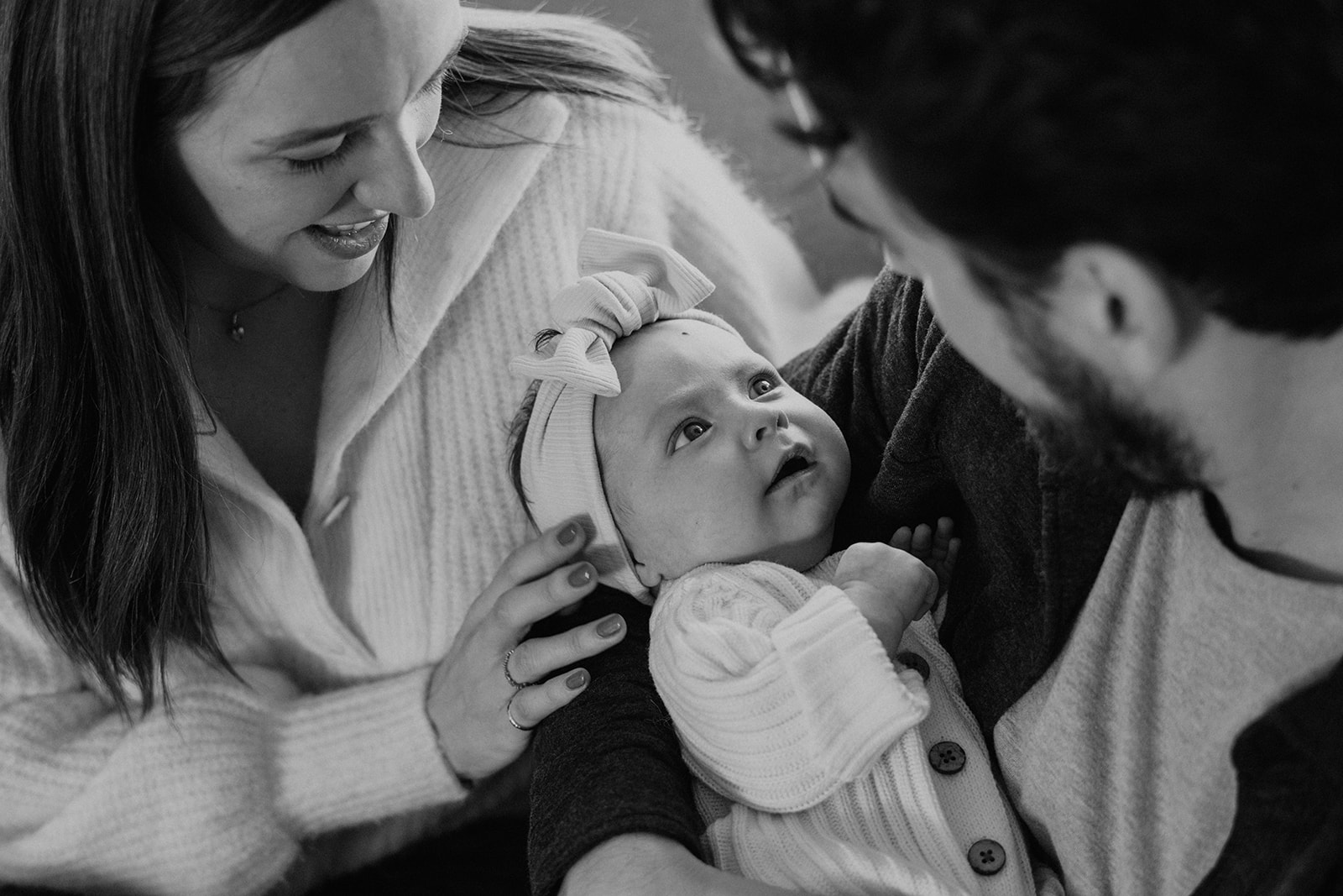 Black and white family photo of newborn baby Nora as she gazes up at her new parents