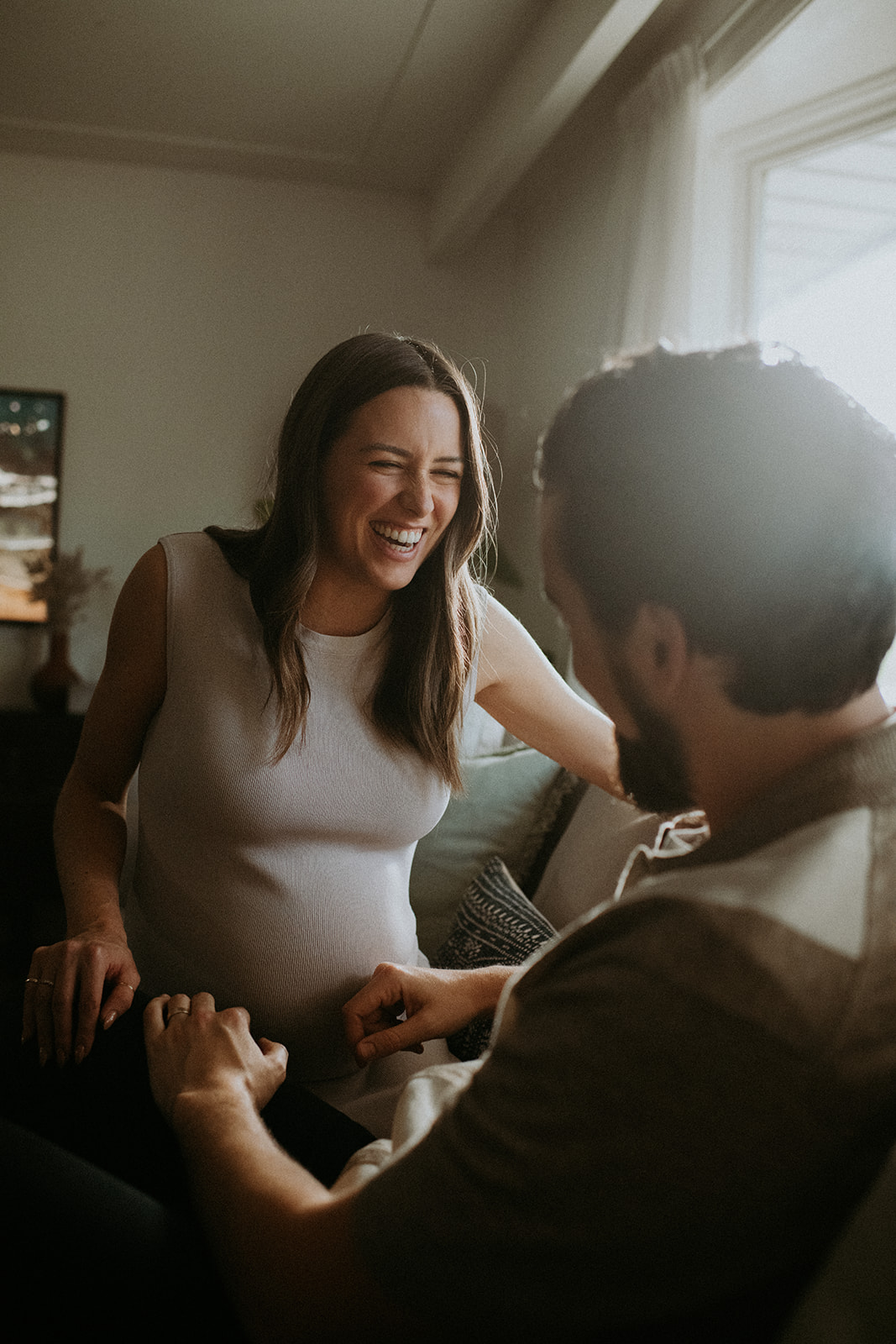 Woman laughs and smiles at her partner during their maternity photoshoot at home