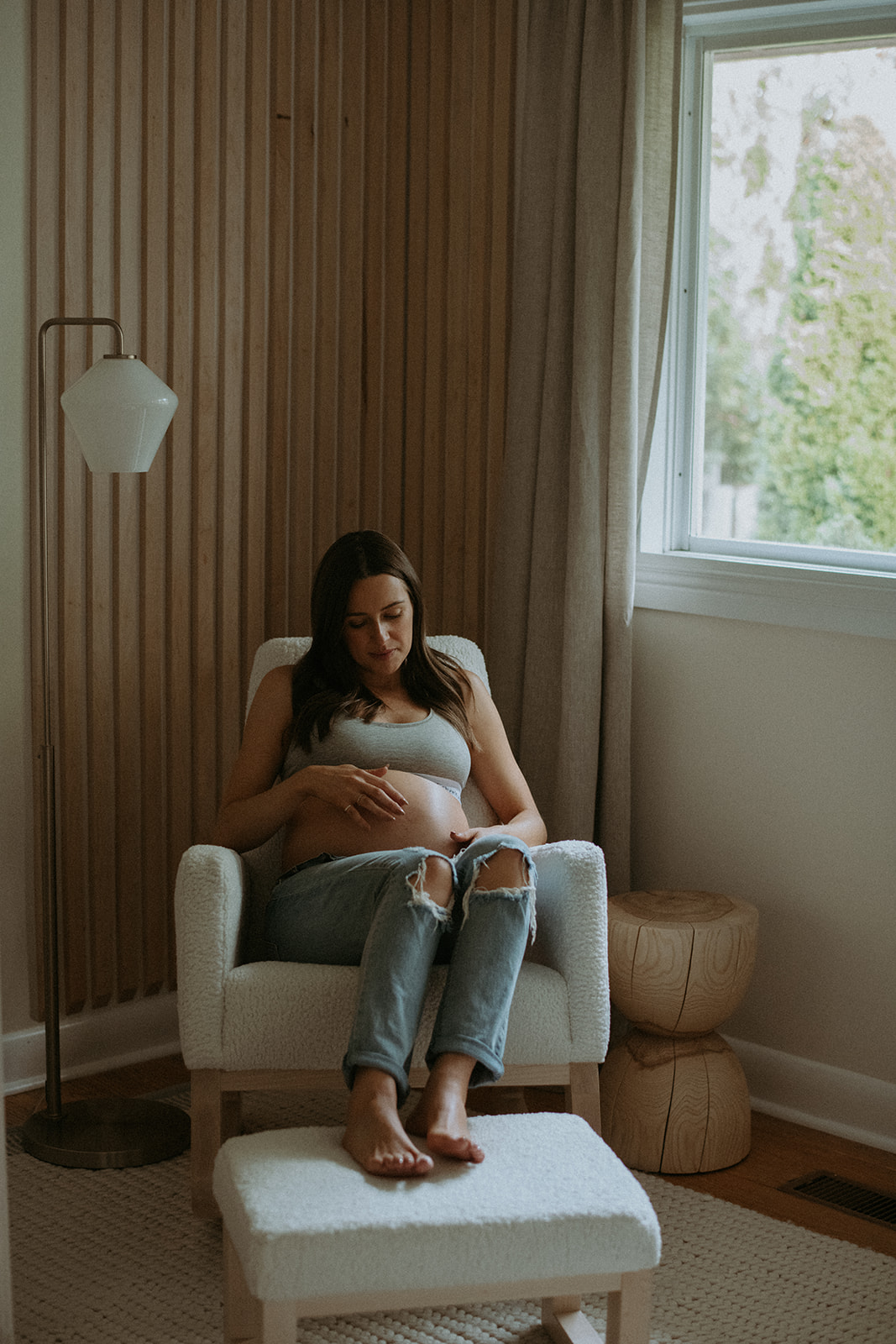Woman gazes down at her pregnant belly for maternity photos in the nursery