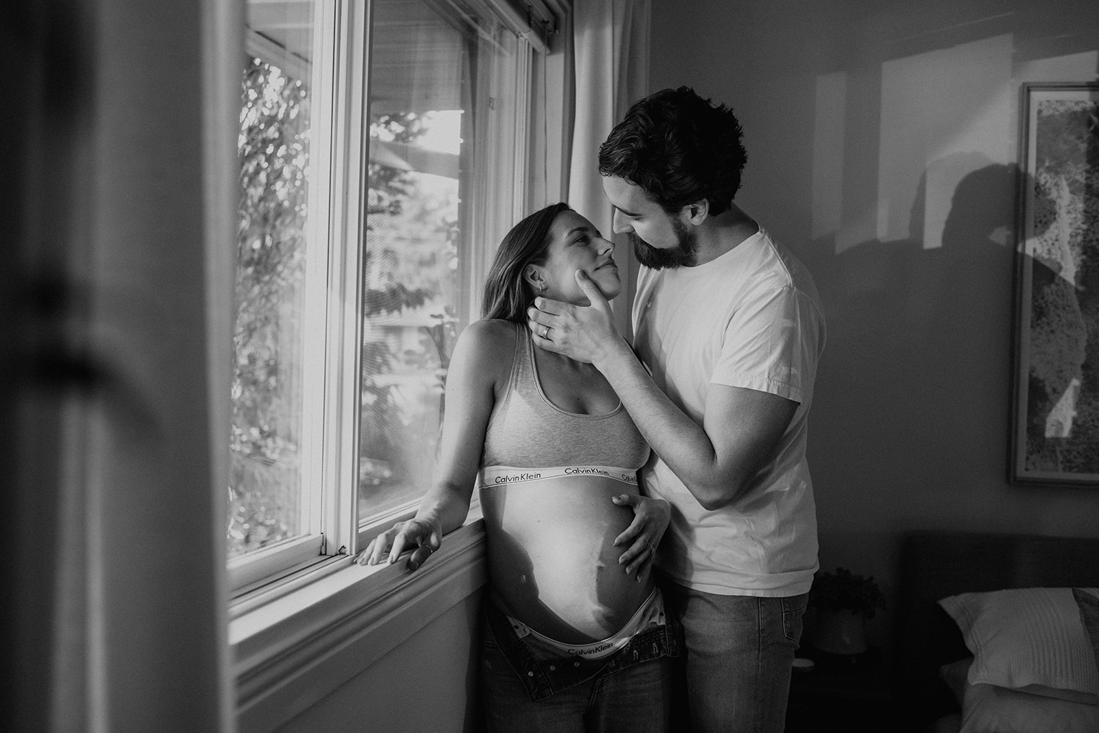 Black and white photo of a couple almost sharing a kiss during their at-home maternity shoot