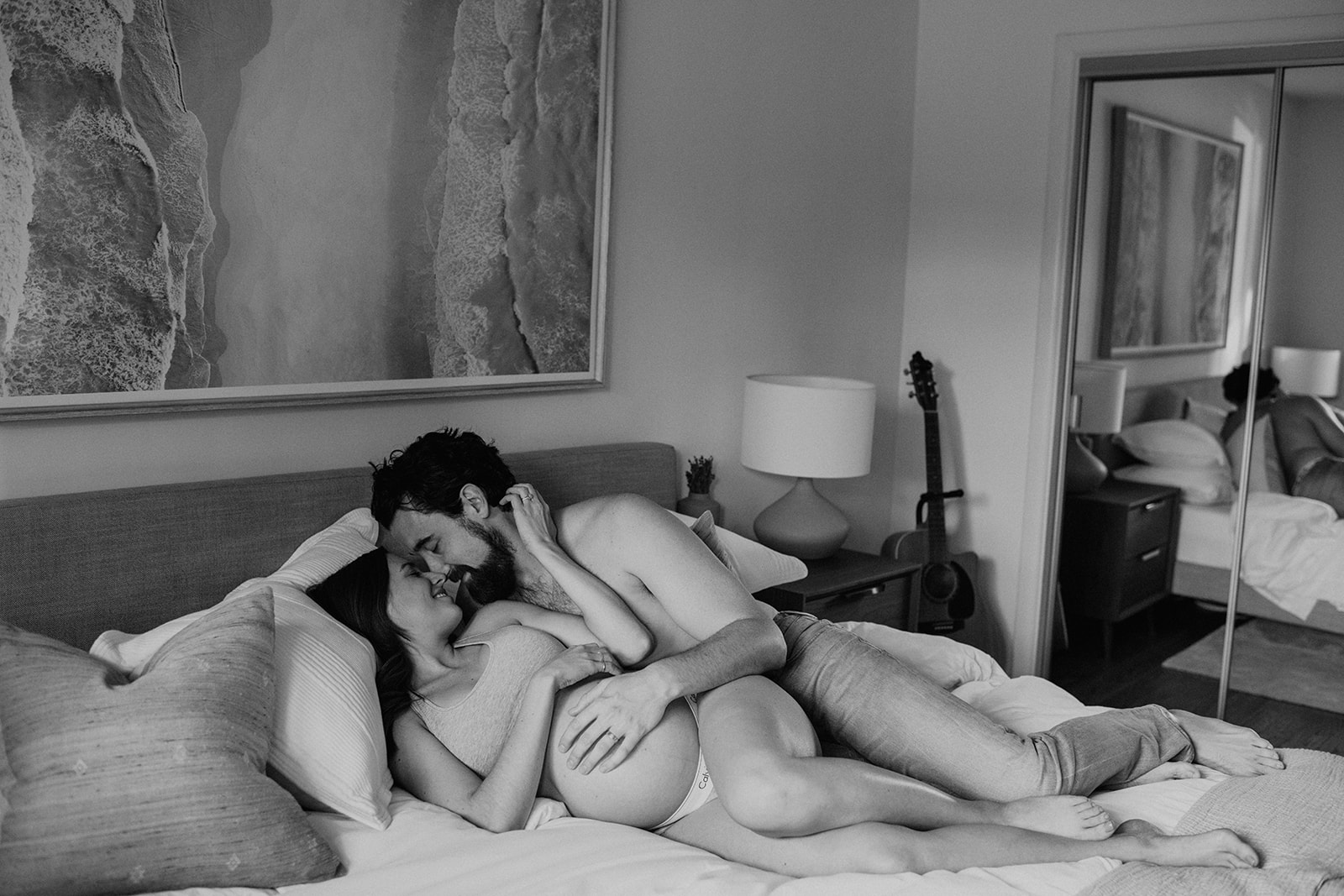 Black and white photo of an expecting couple cuddling in bed taken by their maternity photographer