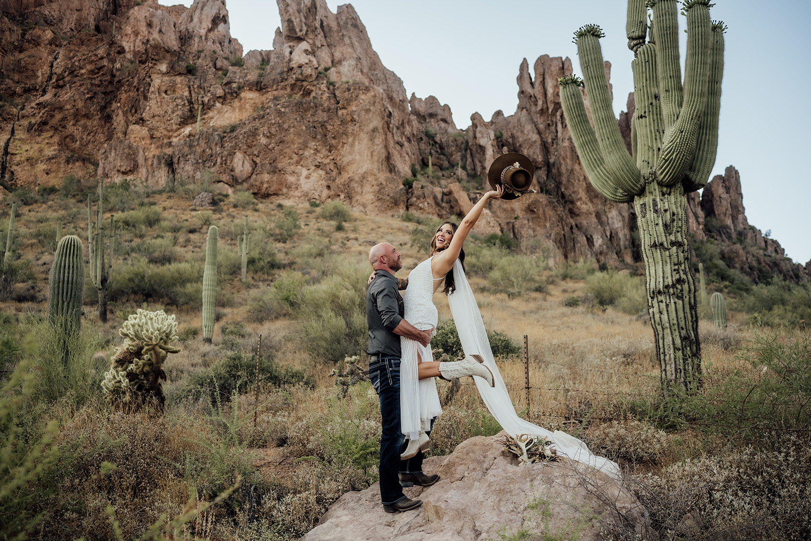 groom holding bride up with superstition mountains and saguaro cactus behind in Gold Canyon, AZ