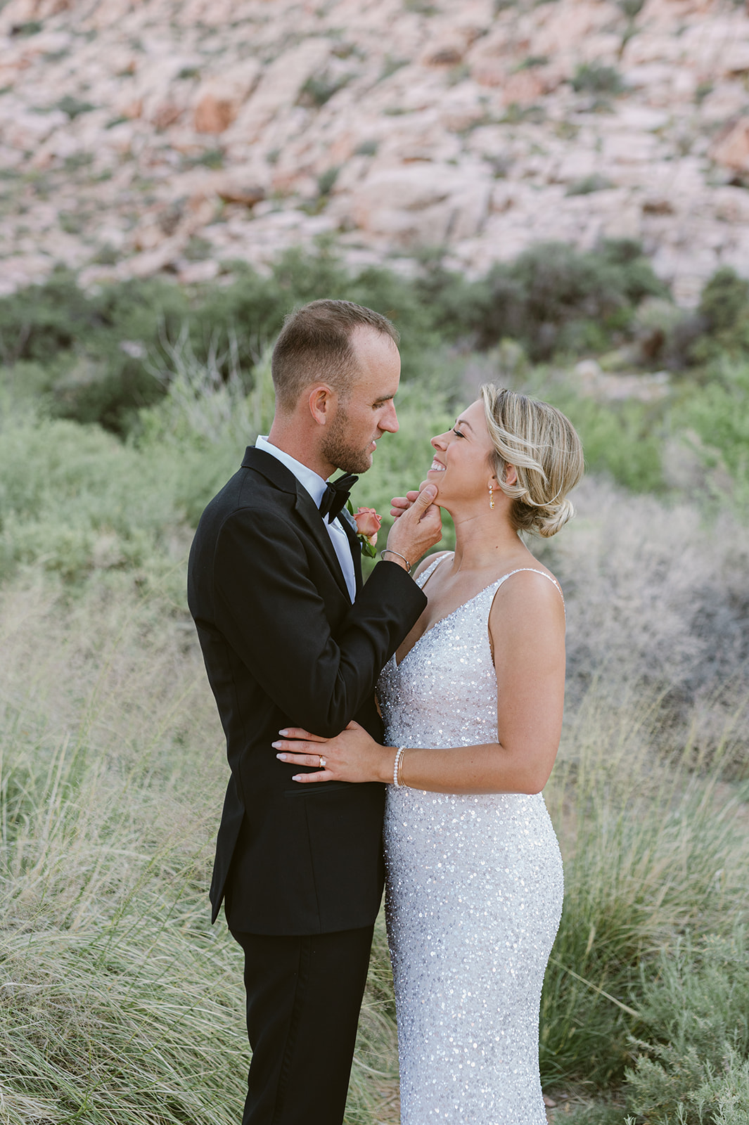 bride and groom embrace on Red Rock Boardwalk with Red Rock Canyon backdrop. Bride wearing glittering white dress.