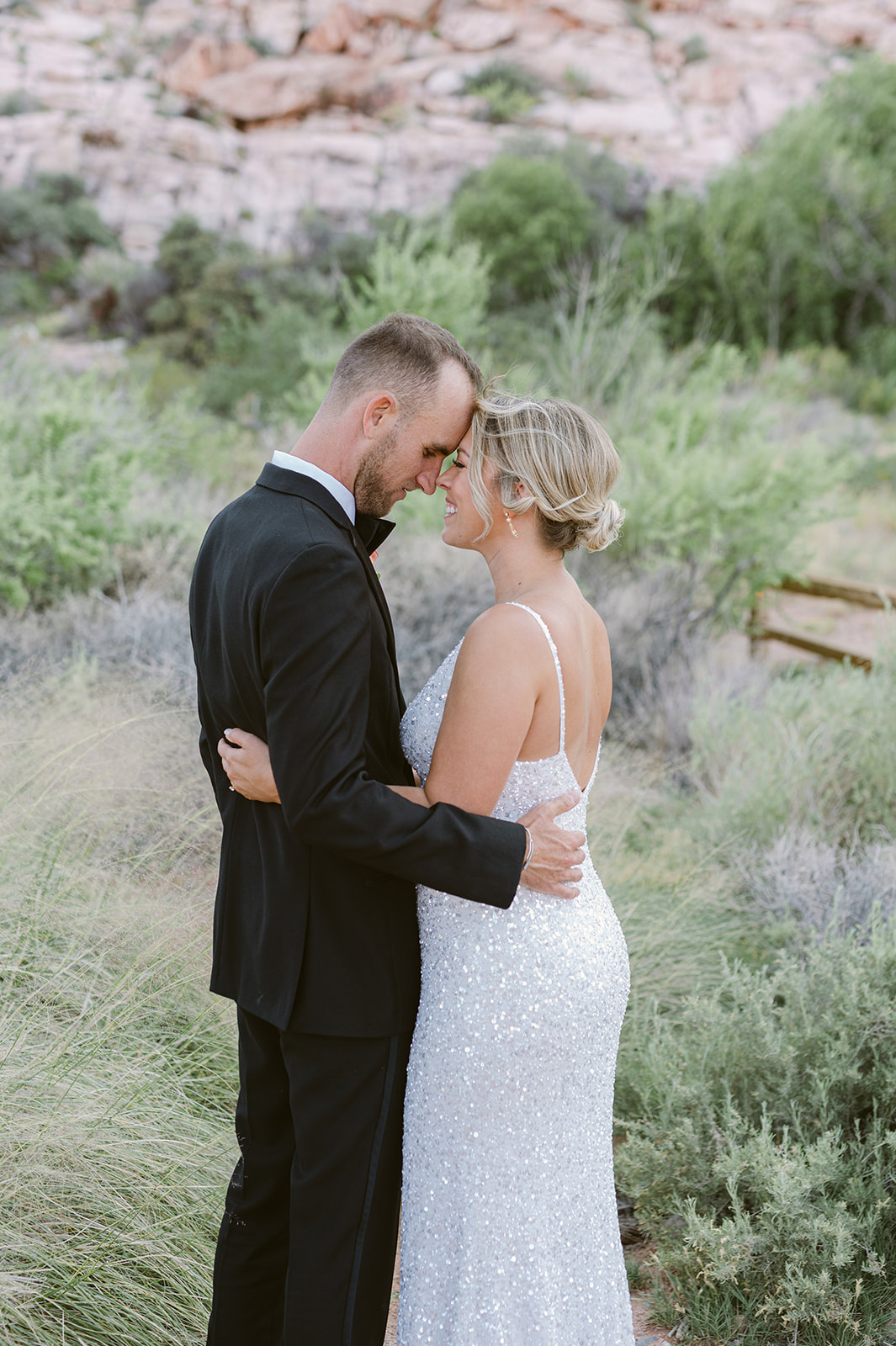 bride and groom embrace on Red Rock Boardwalk with Red Rock Canyon backdrop. Bride wearing glittering white dress.