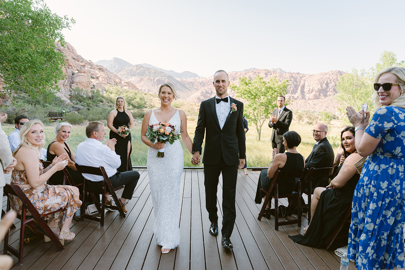 bride and groom walking on Red Rock Boardwalk with Red Rock Canyon backdrop. Bride wearing glittering white dress.