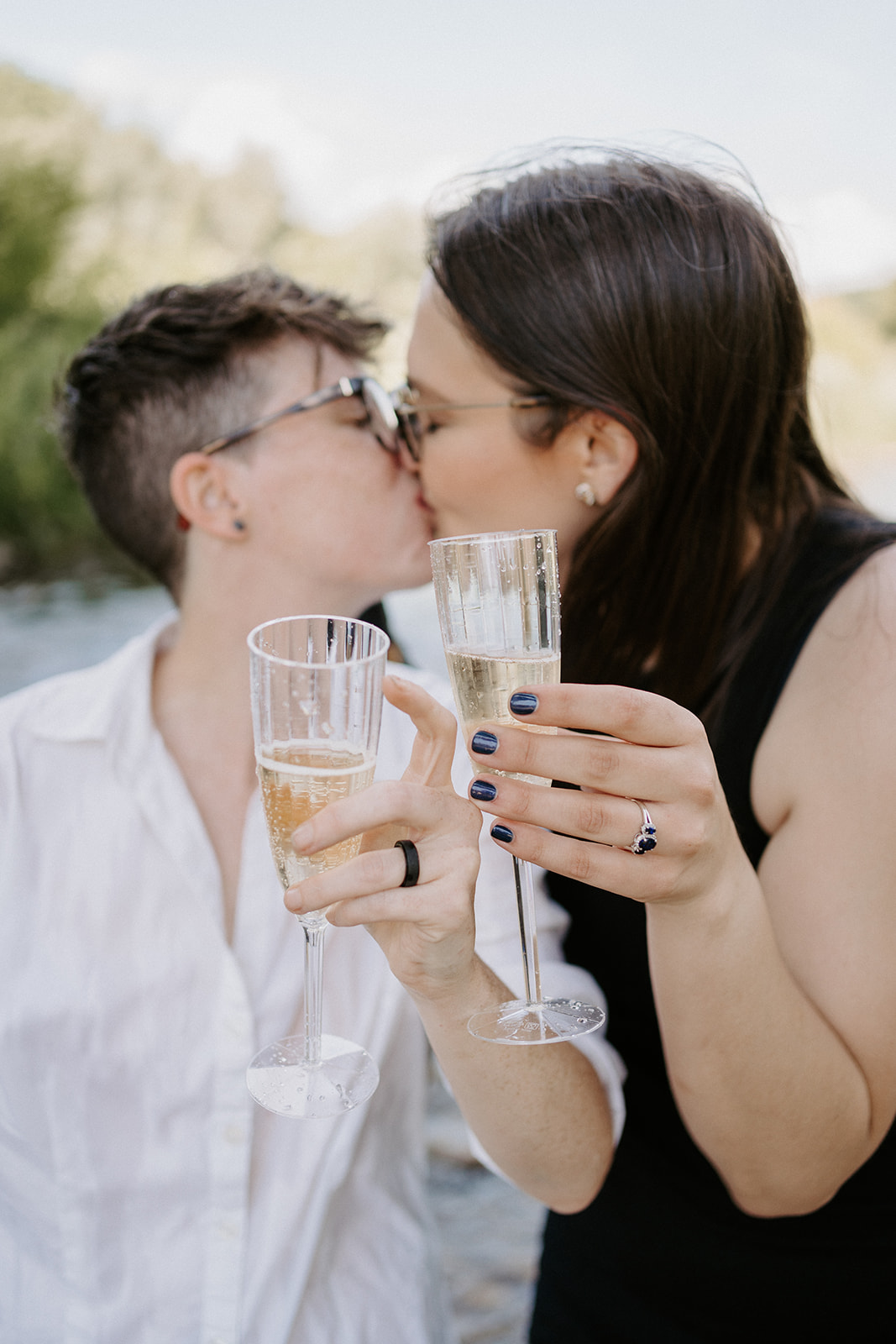 Two people kissing while holding out champagne glasses in front of them.