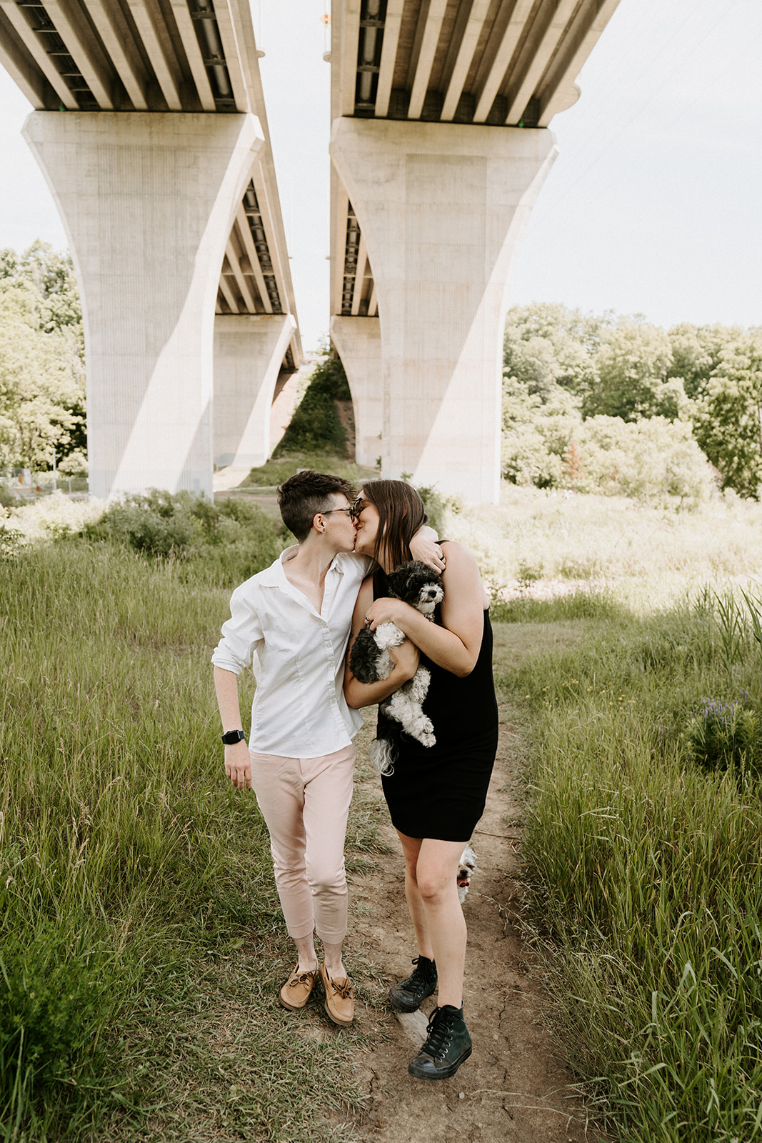 Two people kissing underneath an overpass by the creek.