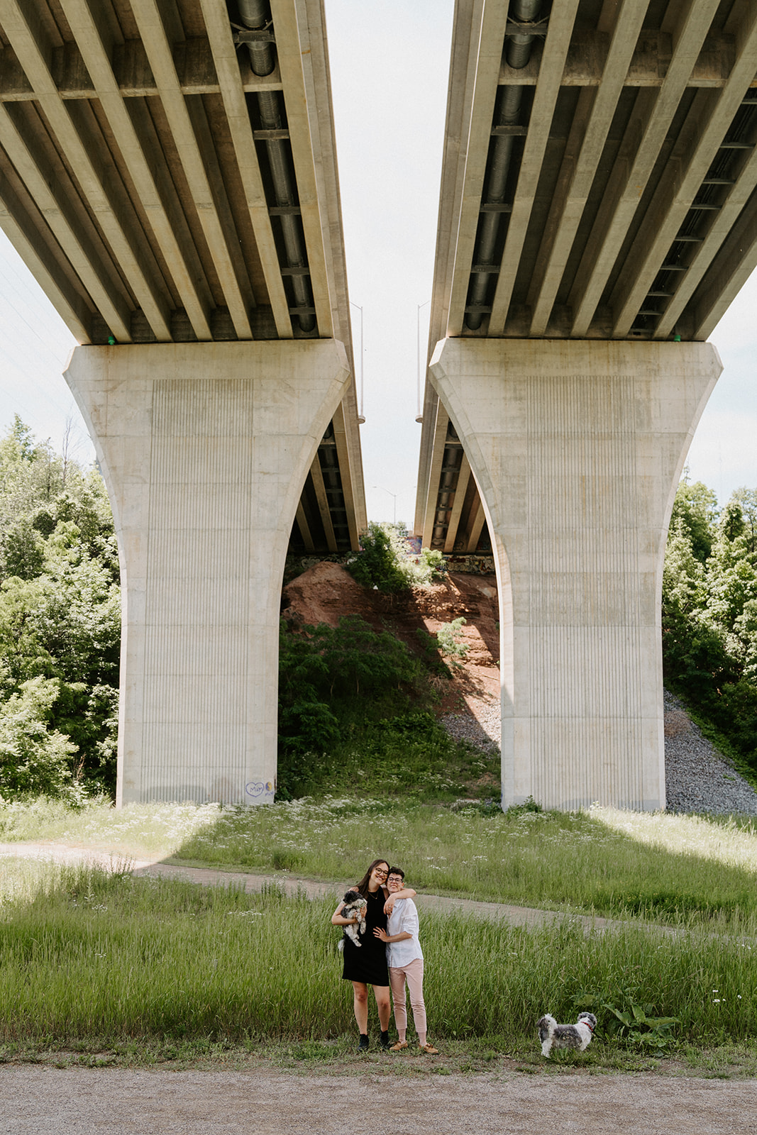 Two people standing underneath an overpass.  One person wrapping their arm around the other.