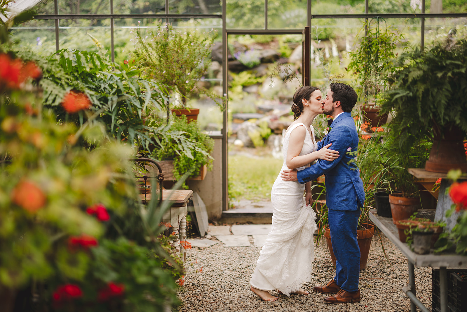 a barefoot bride wearing a white dress hugs her groom in his blue suit inside the greenhouse at Gloriosa & Co. 