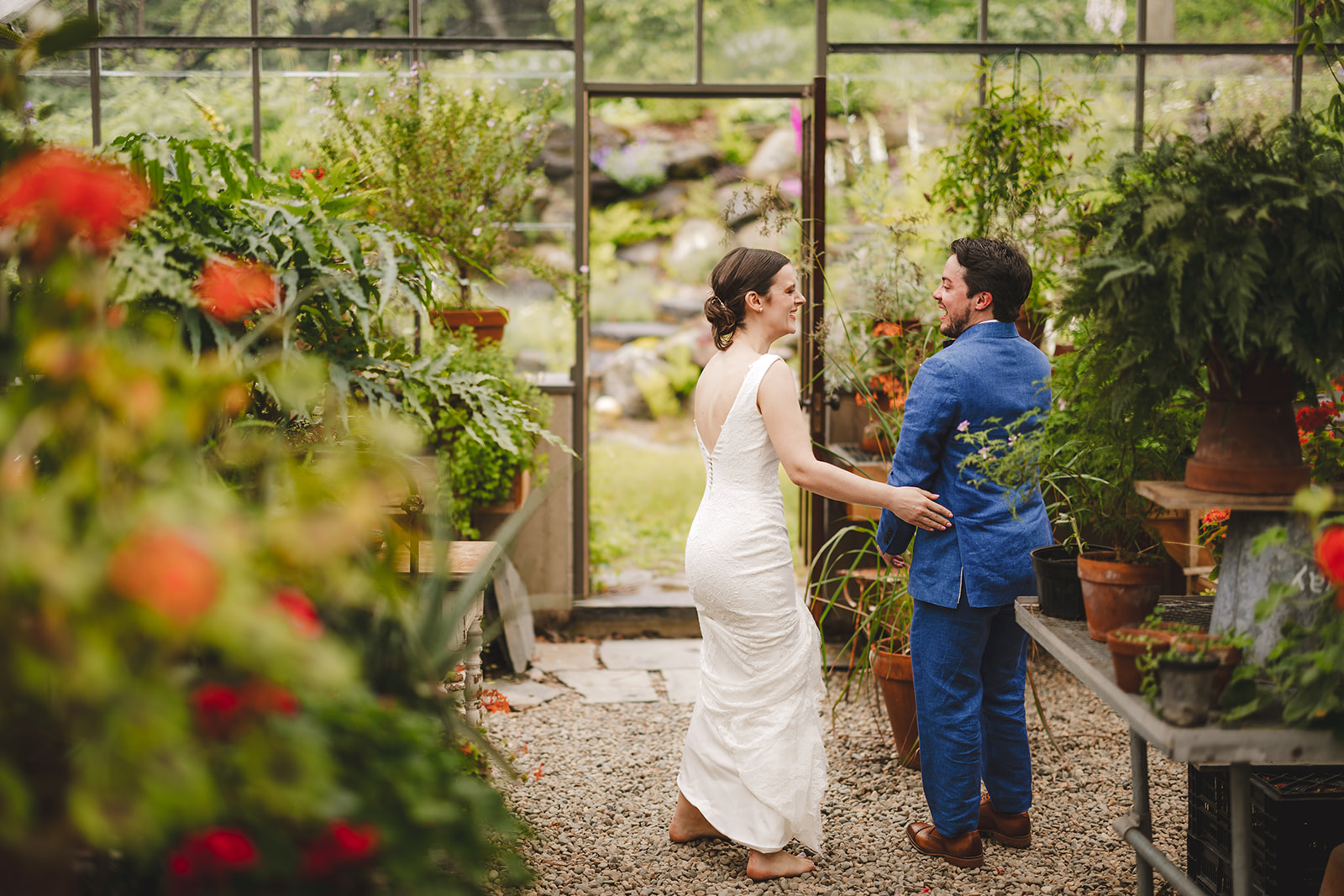 a barefoot bride wearing a white dress surprises her groom in his blue suit inside the greenhouse at Gloriosa & Co. 
