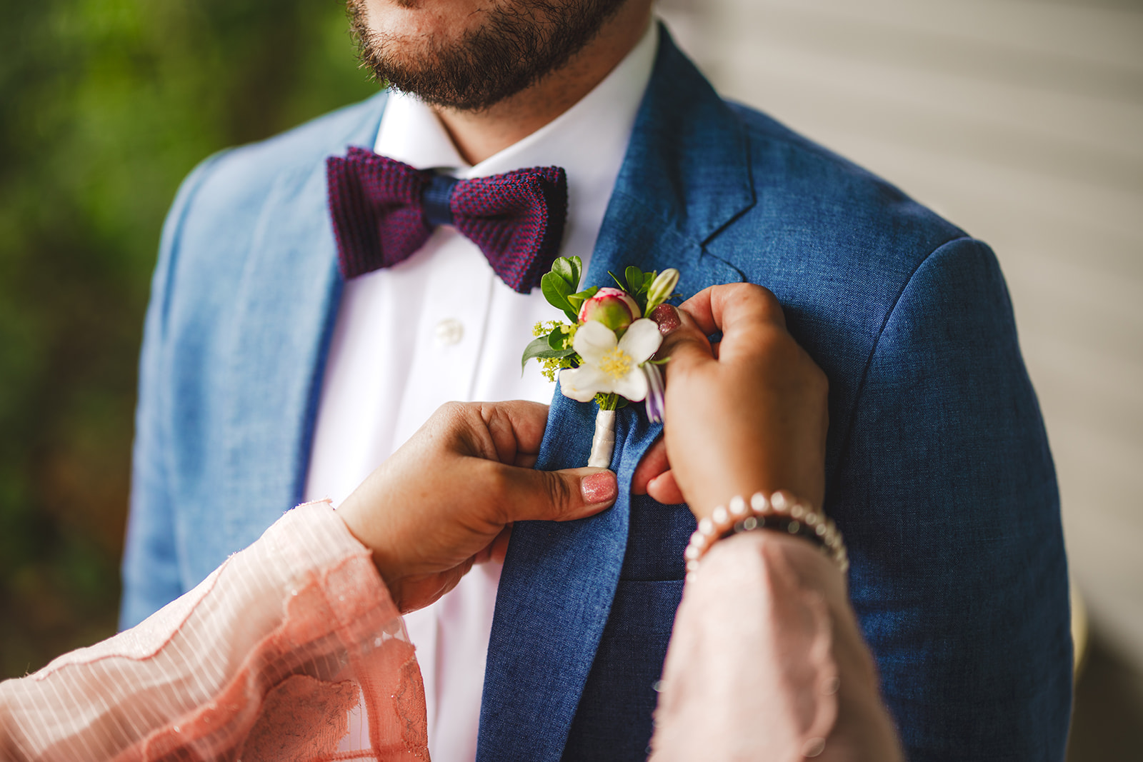 close up of hands fixing a boutonniere on a groom wearing a blue suit and bow tie 