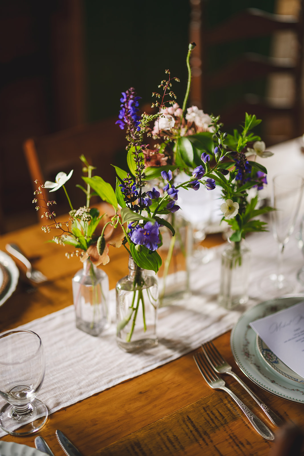 flowers in a vase center piece and place settings on a wooden wedding reception table