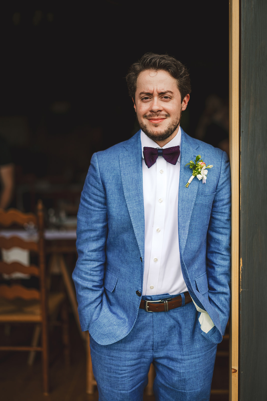 a groom in a blue suit stand in the doorway of a wedding reception barn 