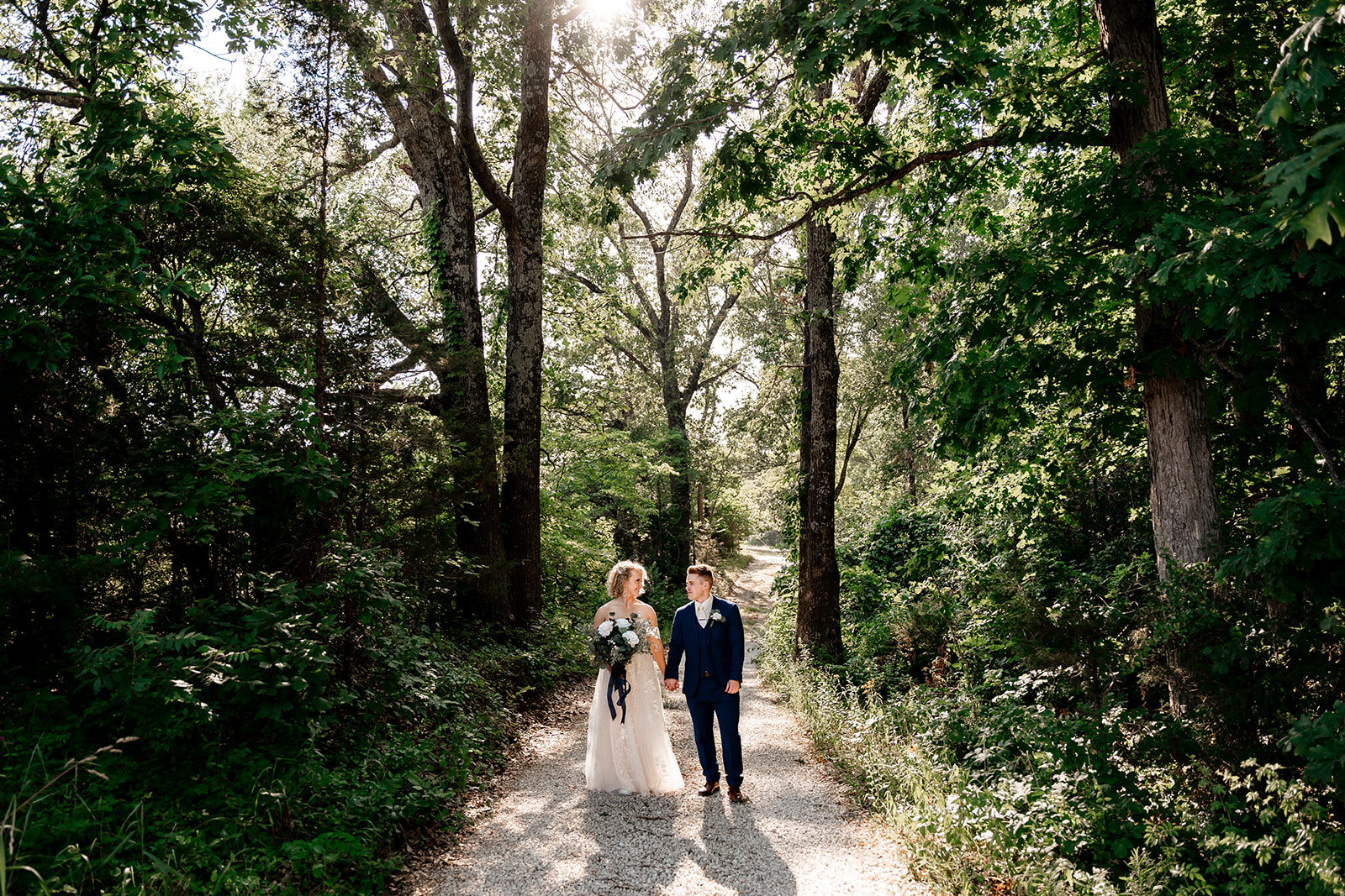 bride and groom walking through woods at sons and daughters venue in rolla mo