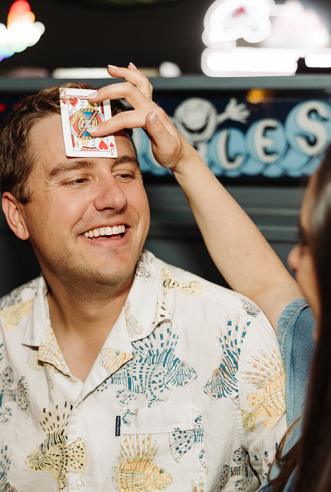 Woman places a playing card on her fiance's forehead while they play a card game at the arcade