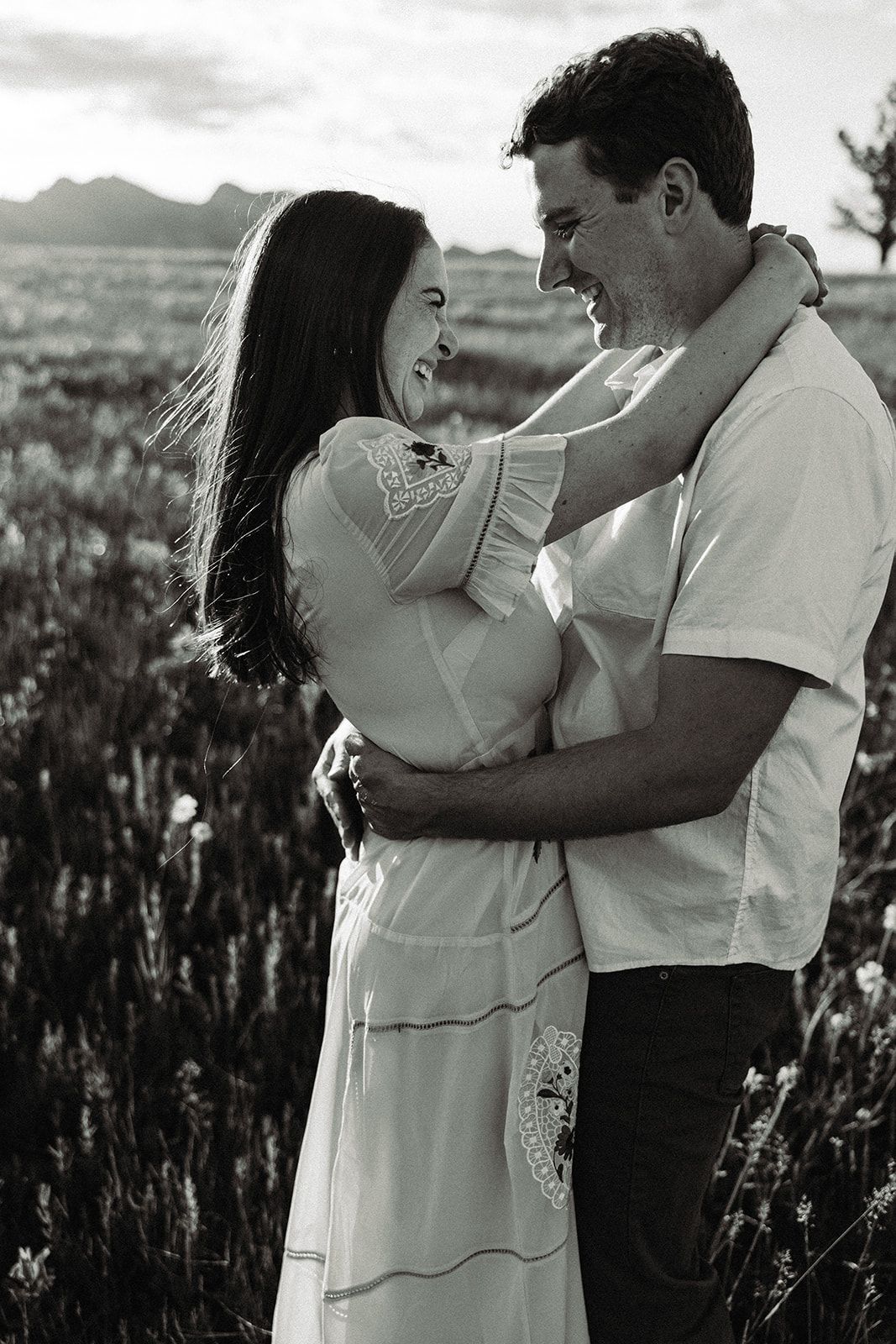 Black and white photo of engaged couple in a field of flowers near a mountain