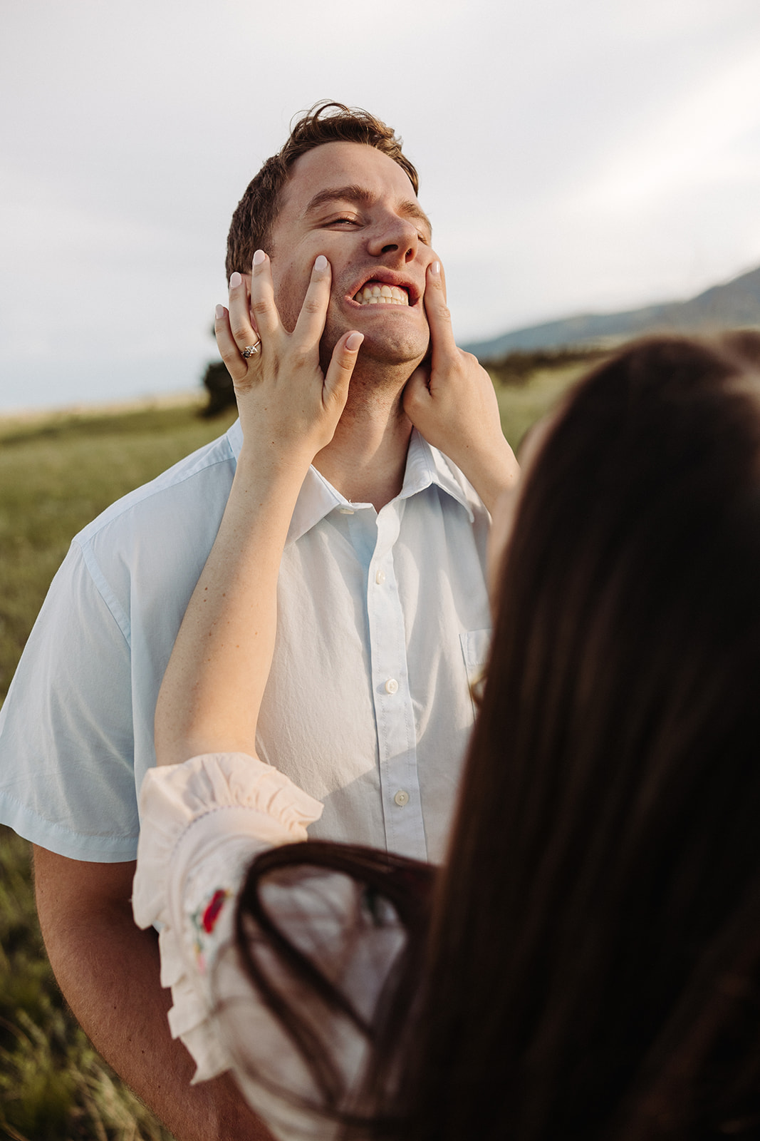 Woman holds her fiance's face as he stretches out his smile, making a silly face