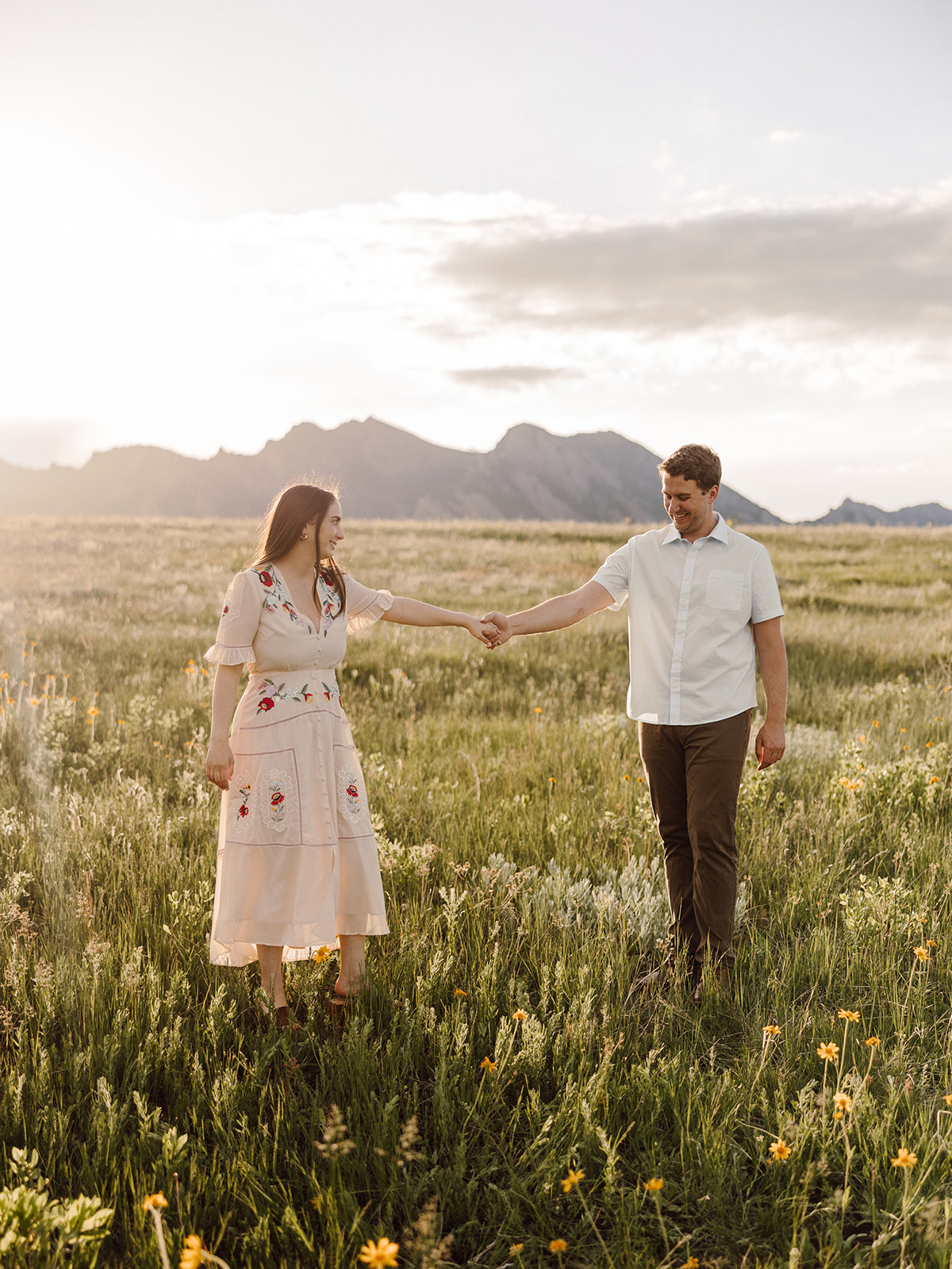Couple holding hands and looking at eachother as they walk towards the camera in a flower field