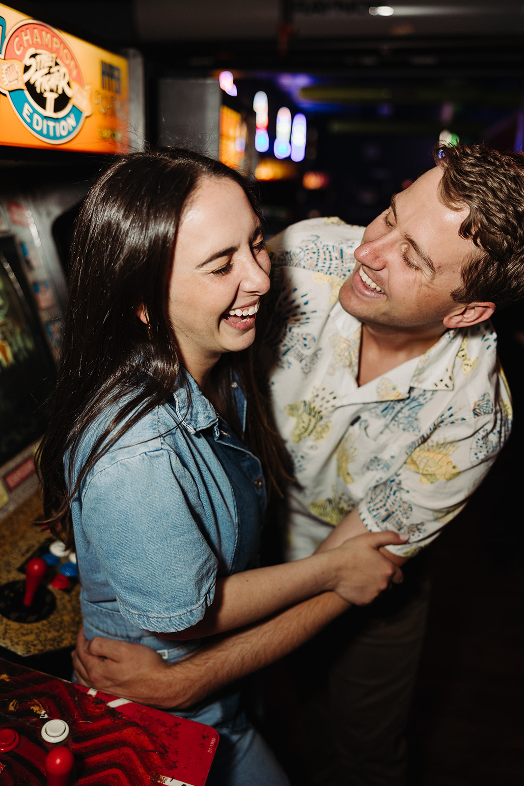 Couple embraces in a hug in front of vintage games during engagement photo session 