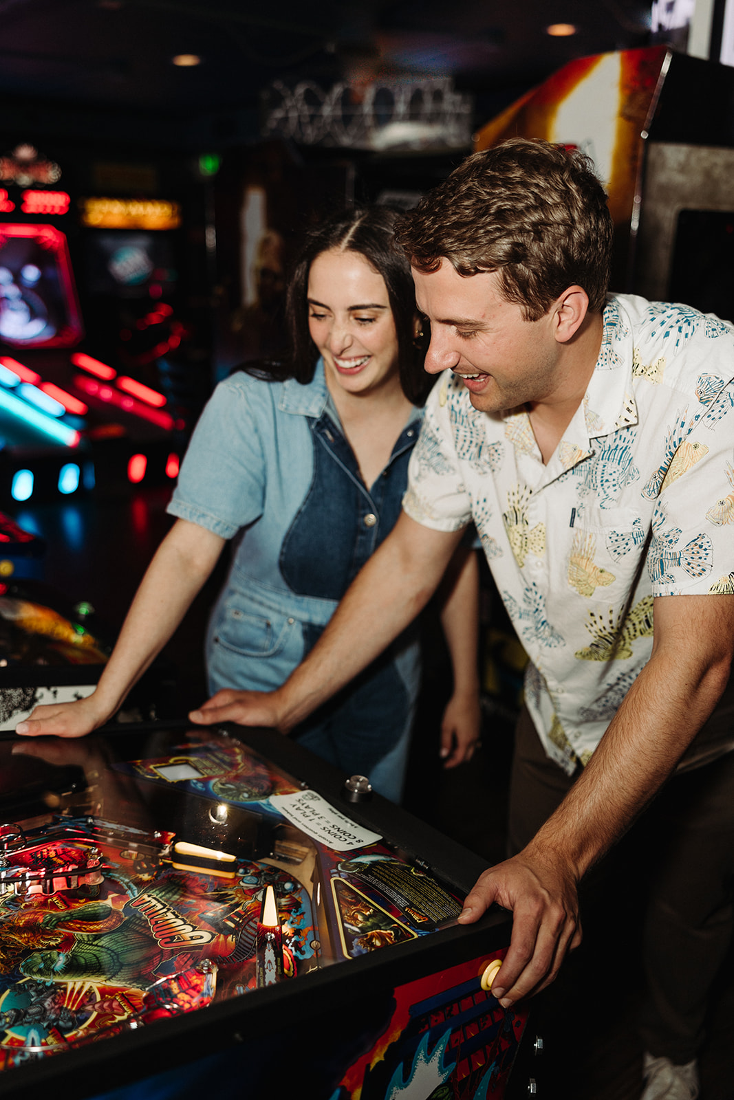 Woman watches her fiance play pinball while laughing