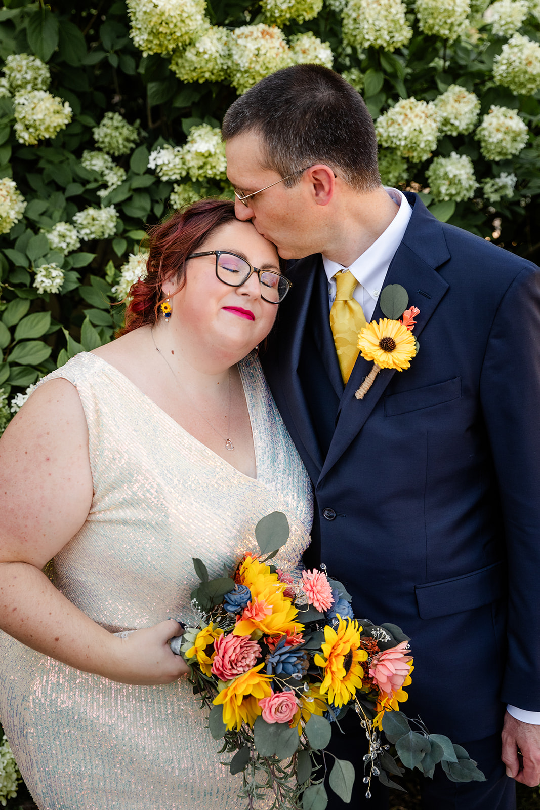 Groom kissing his bride in front of flowers
