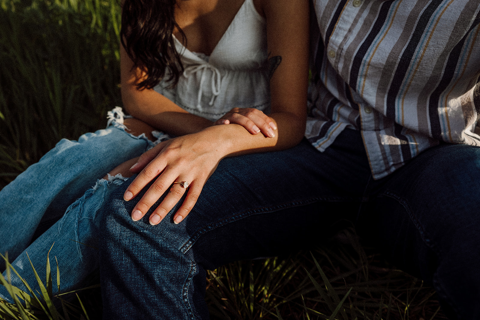 A close up of a woman and man's hands while they sit on the grass 
