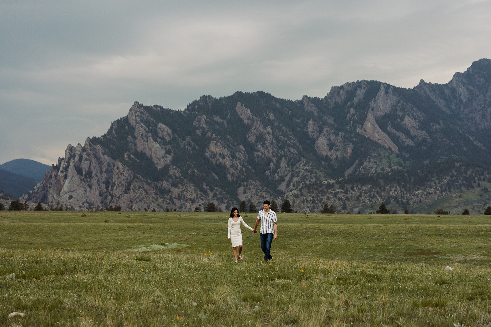 A man and a woman walking along a meadow with mountains in the background 