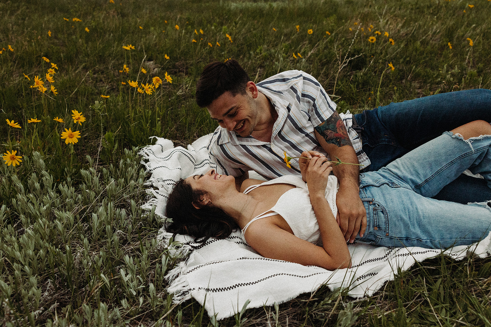 A man and woman lying on a picnic blanket smiling at each other