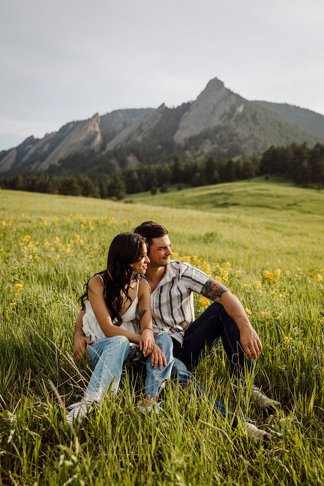 A man and a woman sitting in a meadow with mountains in the background 