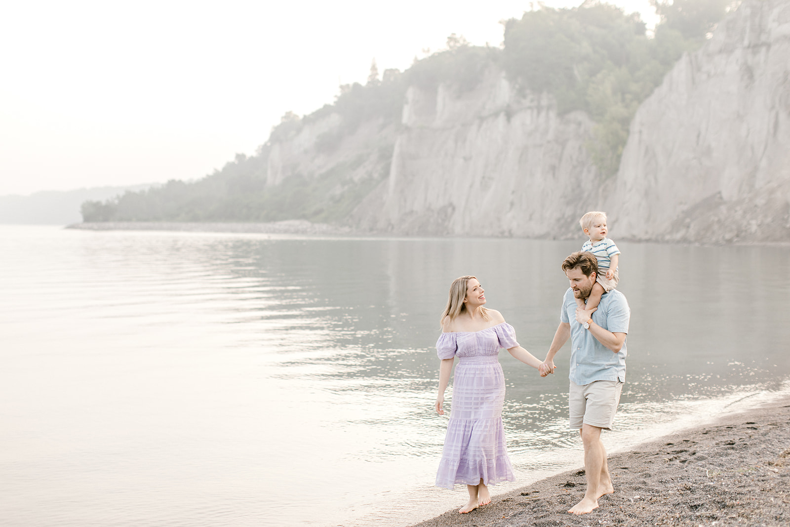 Family holds hands and walks along the beach during their maternity photoshoot 