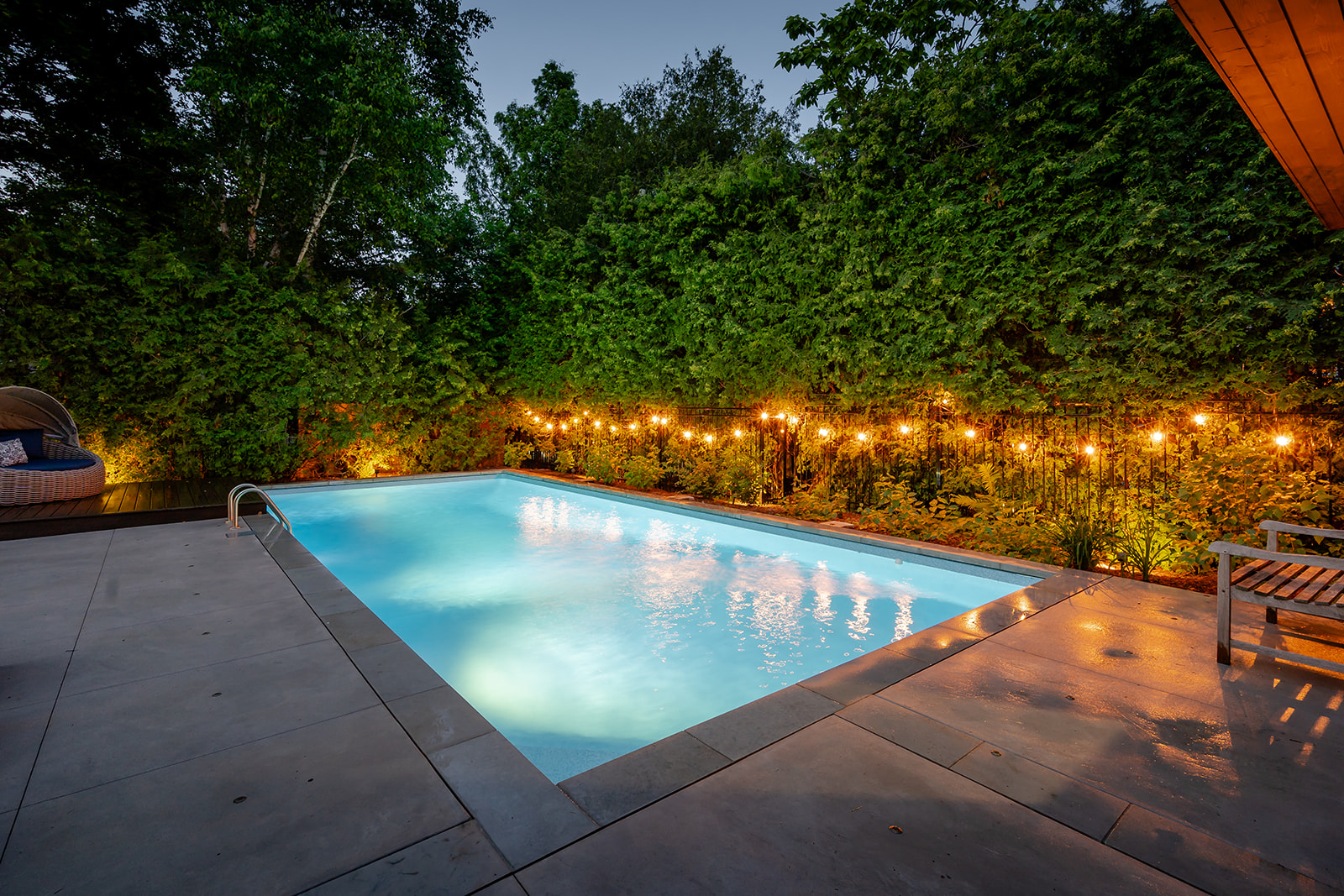 An inground pool with lights on along the gate.