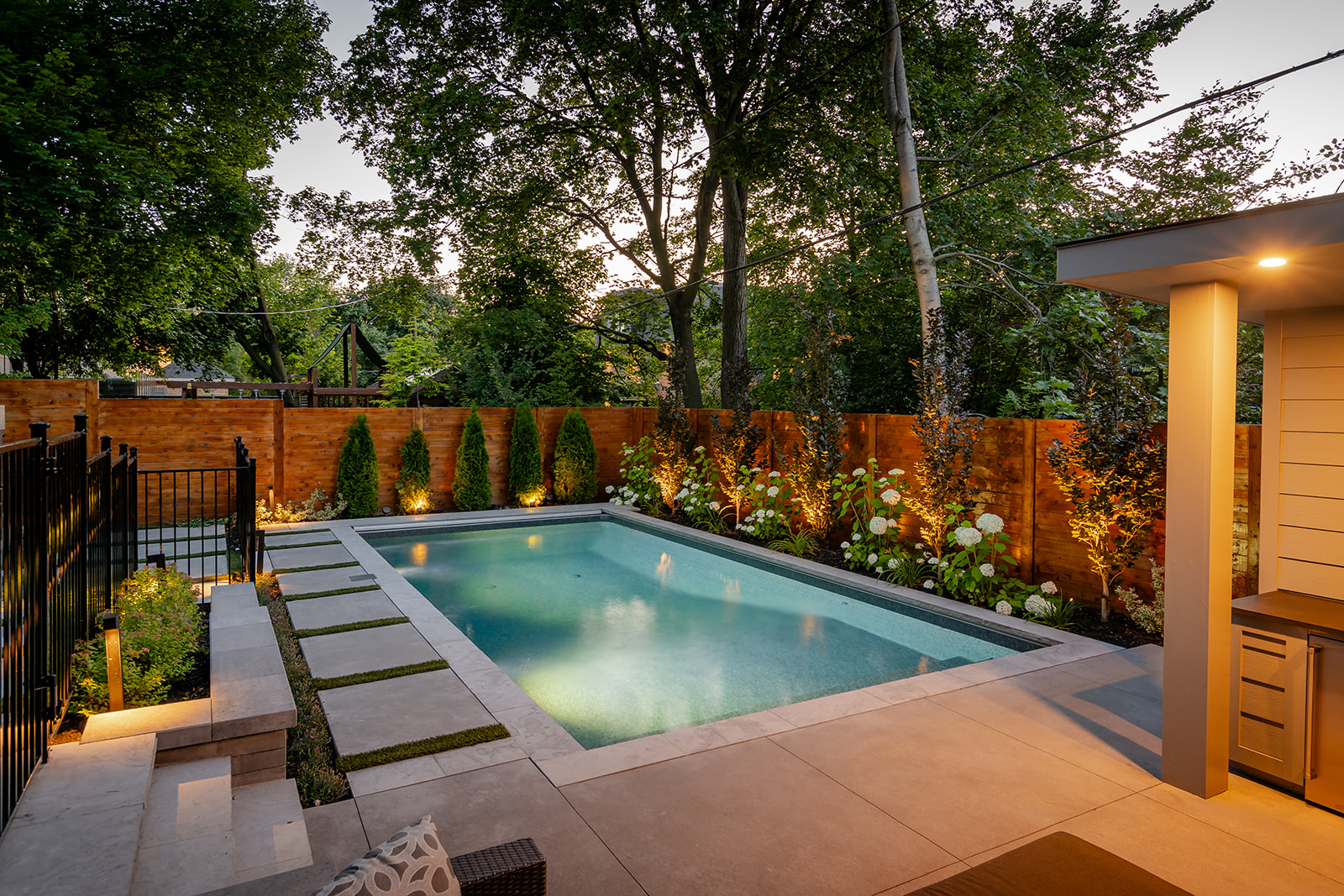 An inground rectangular pool with a garden lining the fence.
