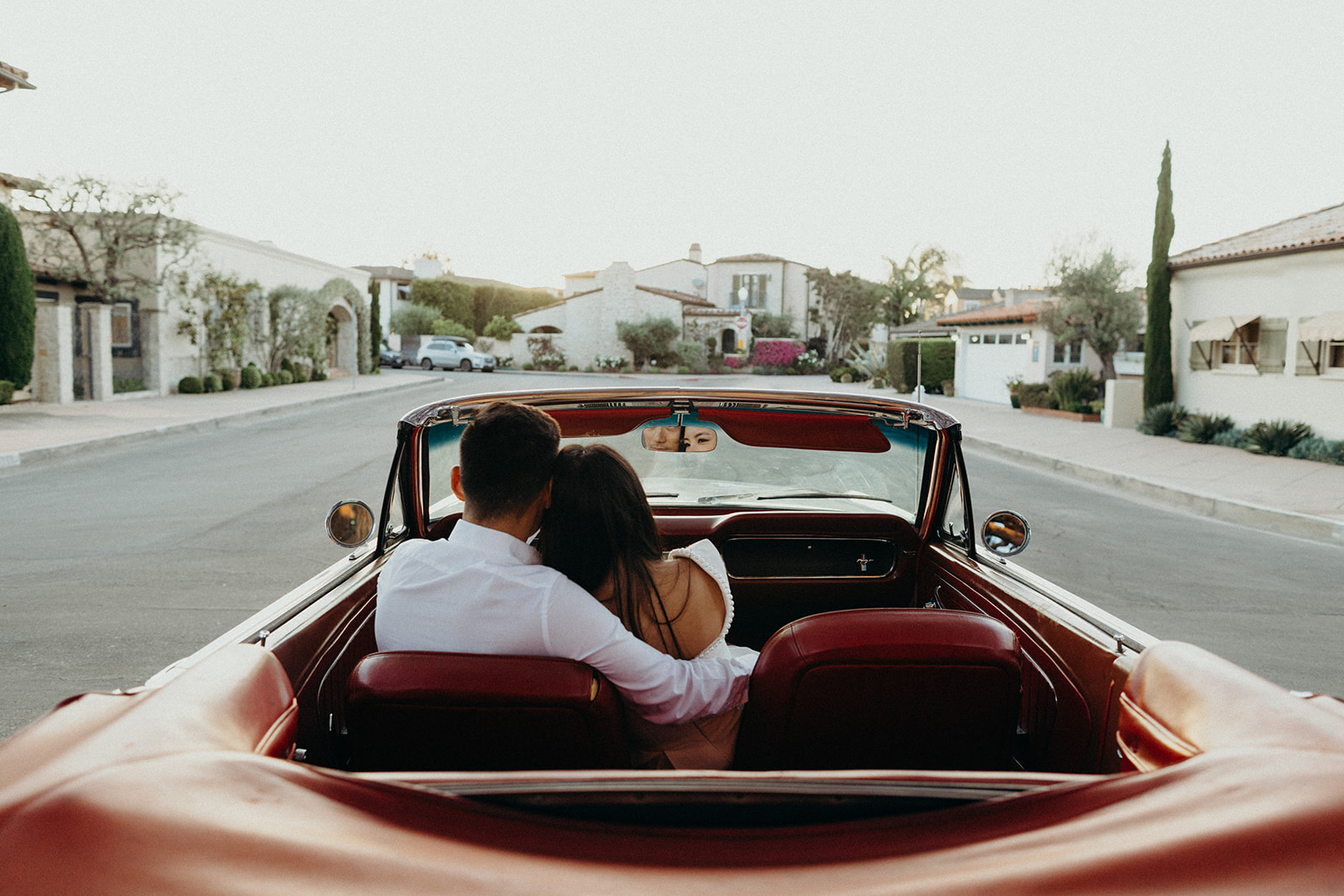 back of head of couple snuggling in a vintage mustang with red leather seats