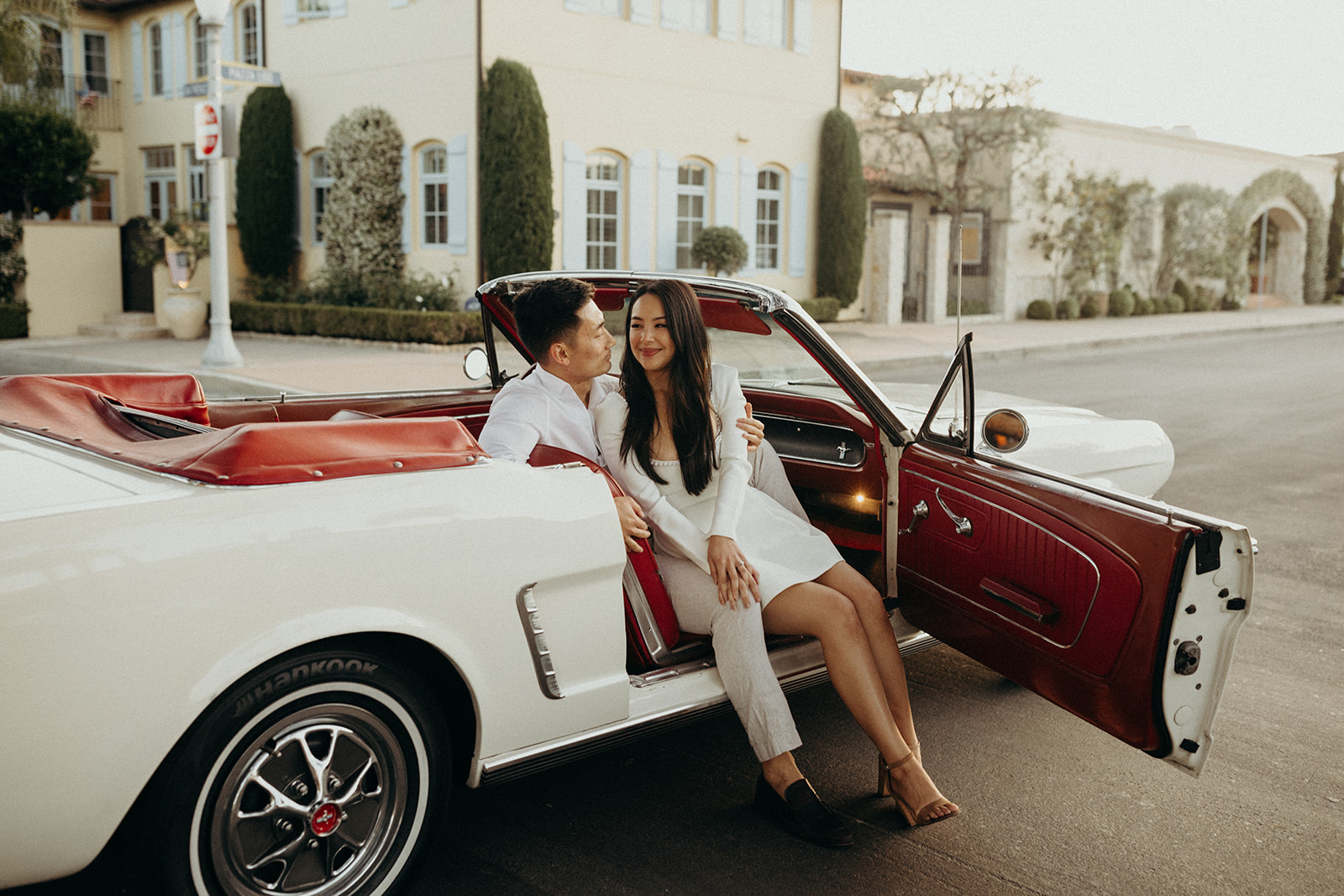 couple dressed in white sitting inside a white vintage mustang with red leather seats