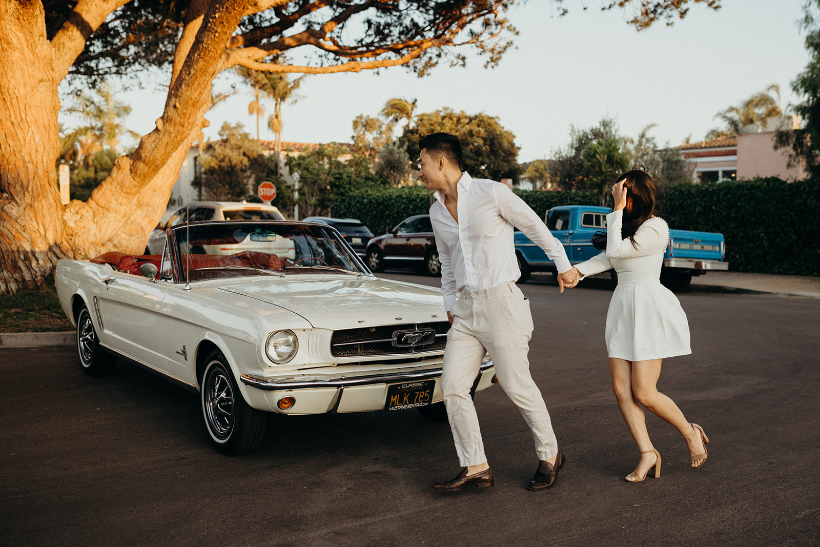 couple holding hands running towards a white vintage mustang