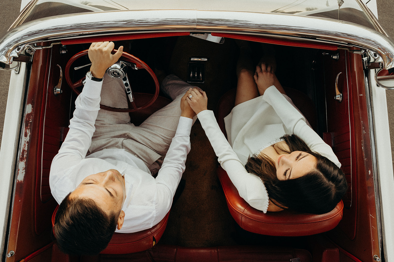 top view of couple holding hands sitting inside a vintage car with red leather seats